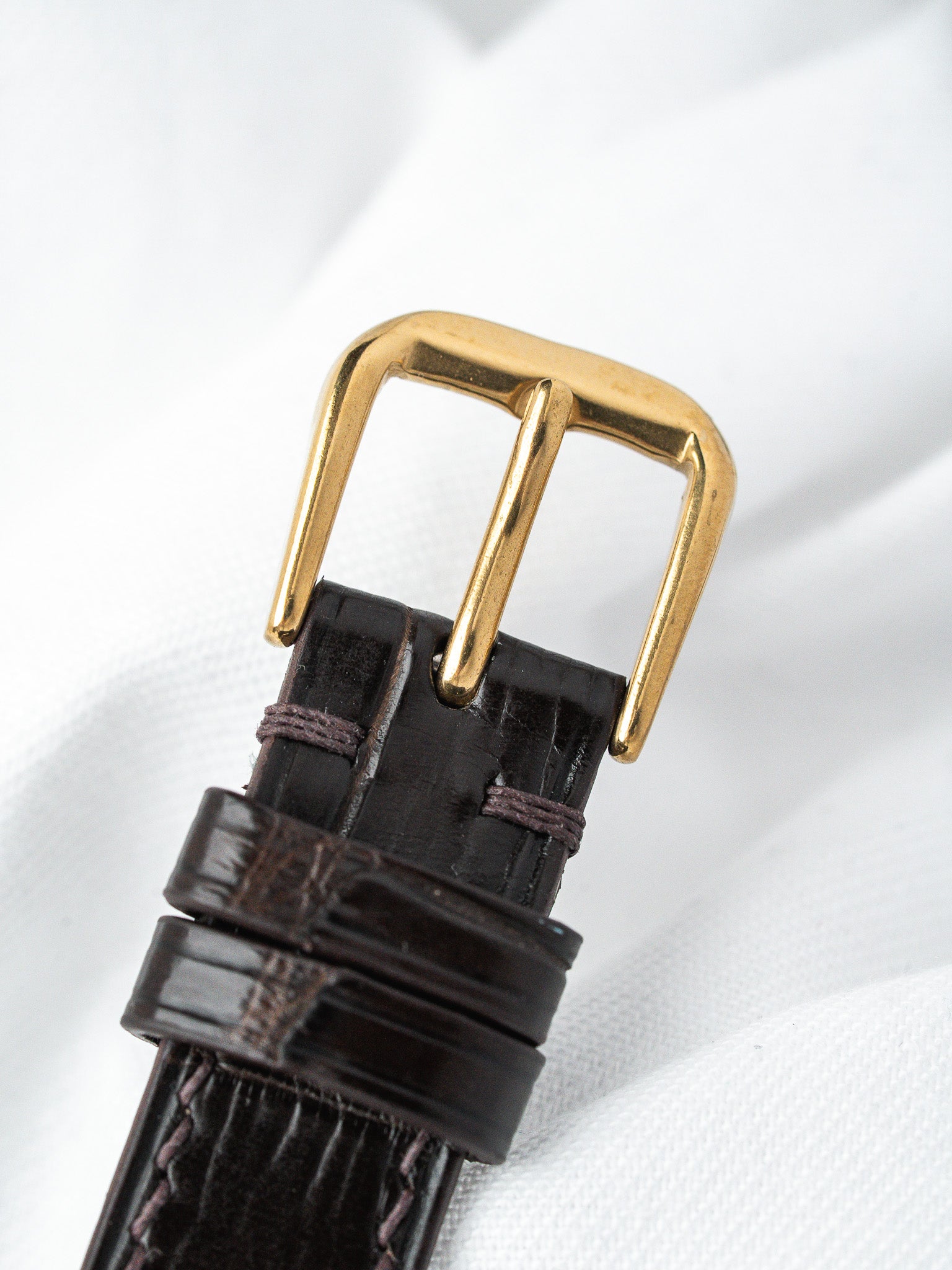 Vintage watch strap with brown alligator leather and gold buckle on white fabric