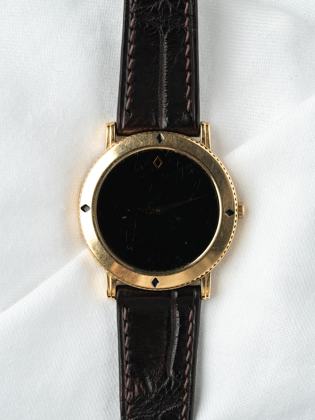 Montre vintage au boîtier rond doré, cadran noir et bracelet en cuir marron