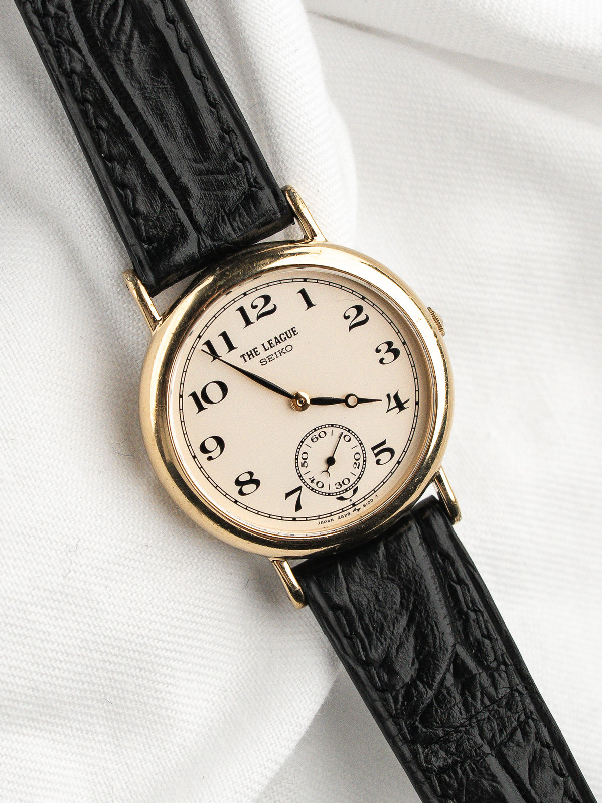 Montre vintage Seiko The League avec cadran crème et bracelet en cuir noir.