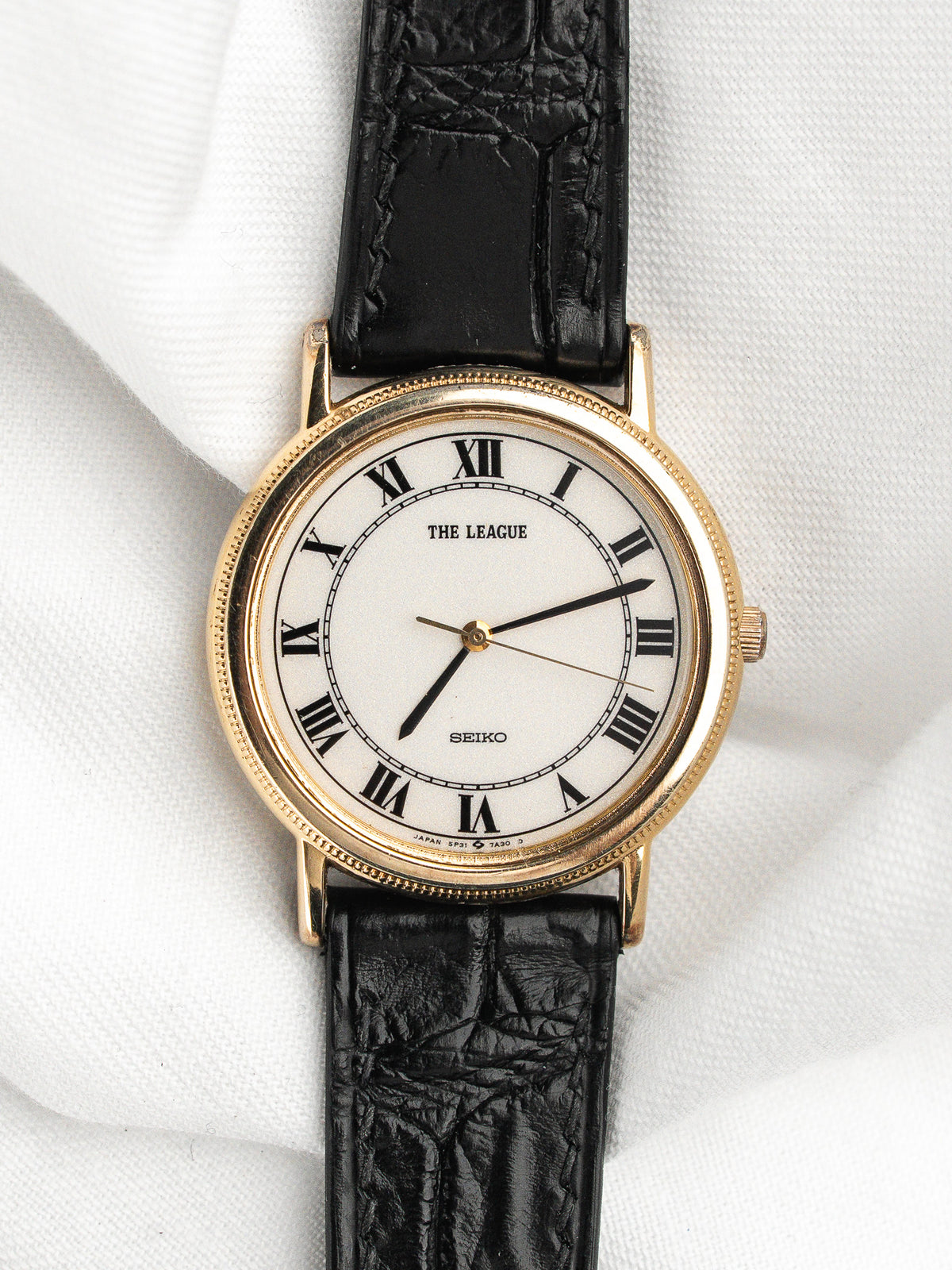 Montre Seiko vintage avec cadran blanc, chiffres romains et bracelet en cuir noir.