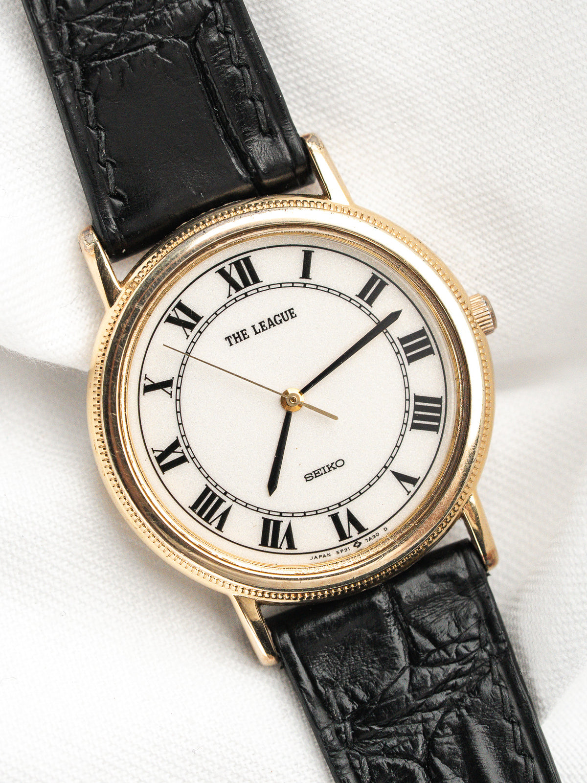 Montre Seiko vintage au cadran blanc avec chiffres romains et bracelet cuir noir.