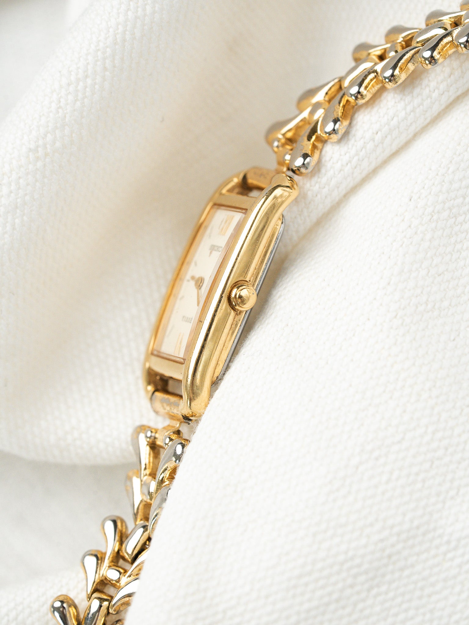 Cartier Tank vintage watch with gold case, white dial, and two-tone bracelet on white fabric