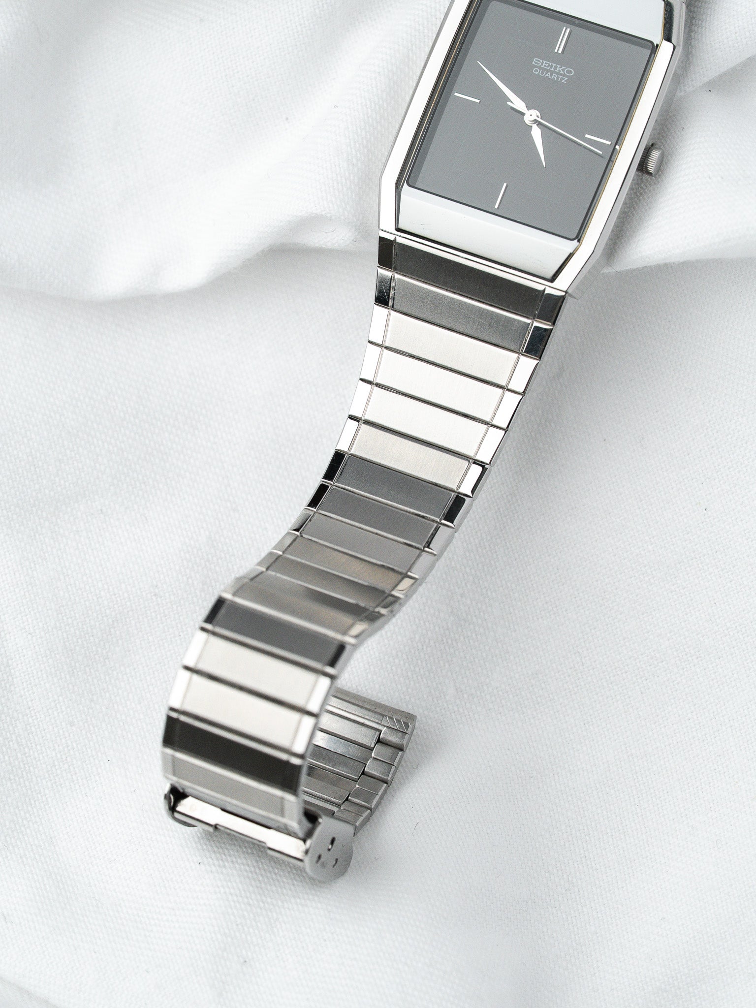 Seiko Quartz vintage watch with rectangular case, grey dial, and steel bracelet on white fabric