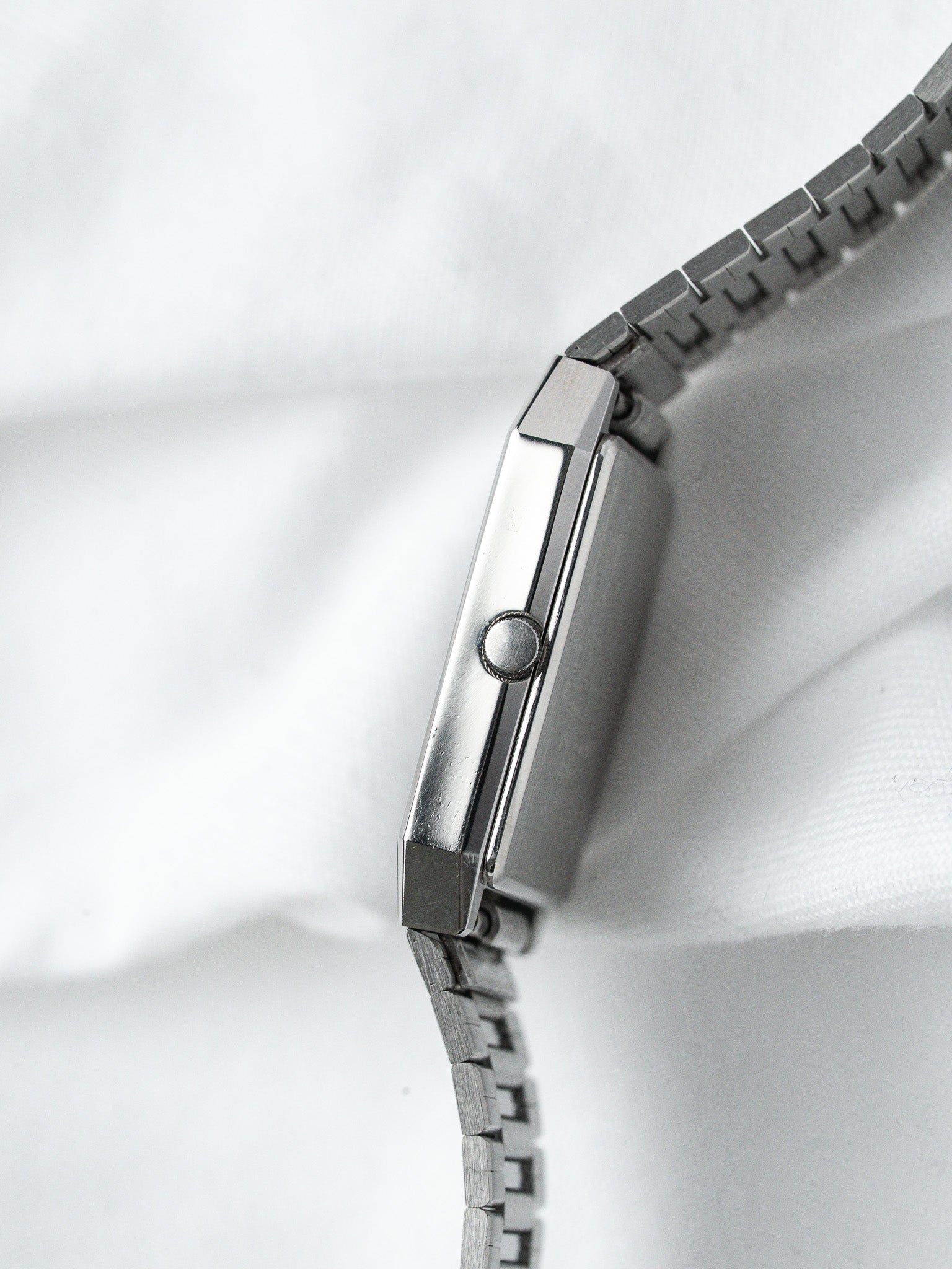 Vintage Omega rectangular steel watch with integrated bracelet, side profile on white fabric