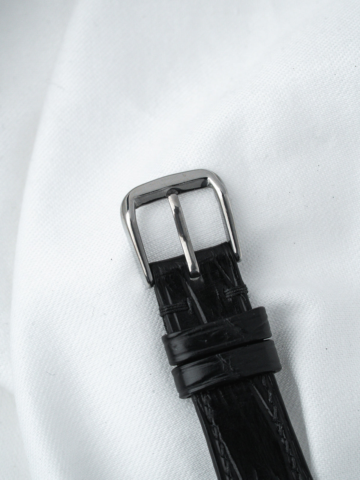 Black alligator leather watch strap with polished steel buckle on white fabric