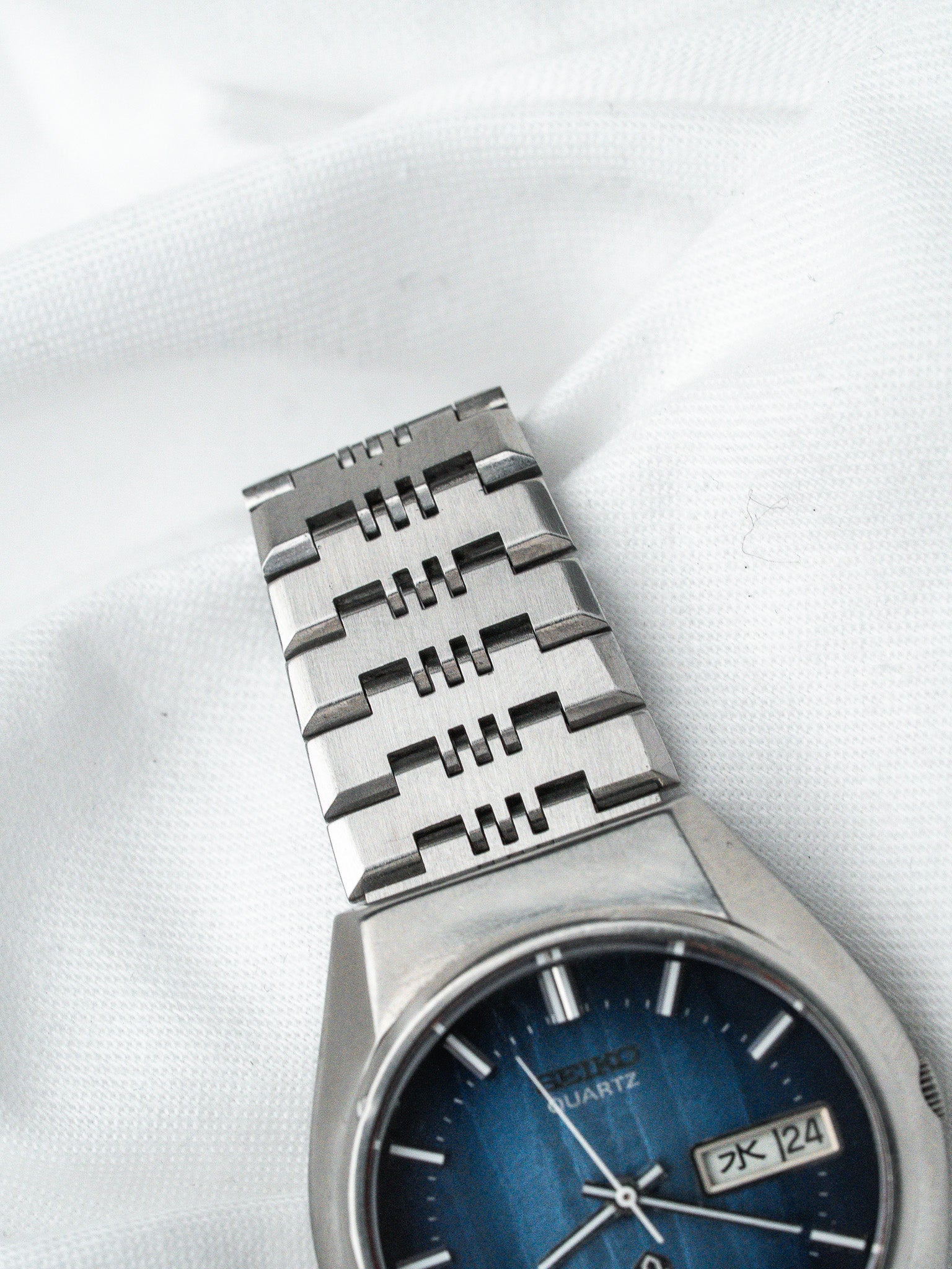 Seiko Quartz vintage watch with blue dial, day-date window, and steel bracelet on white fabric