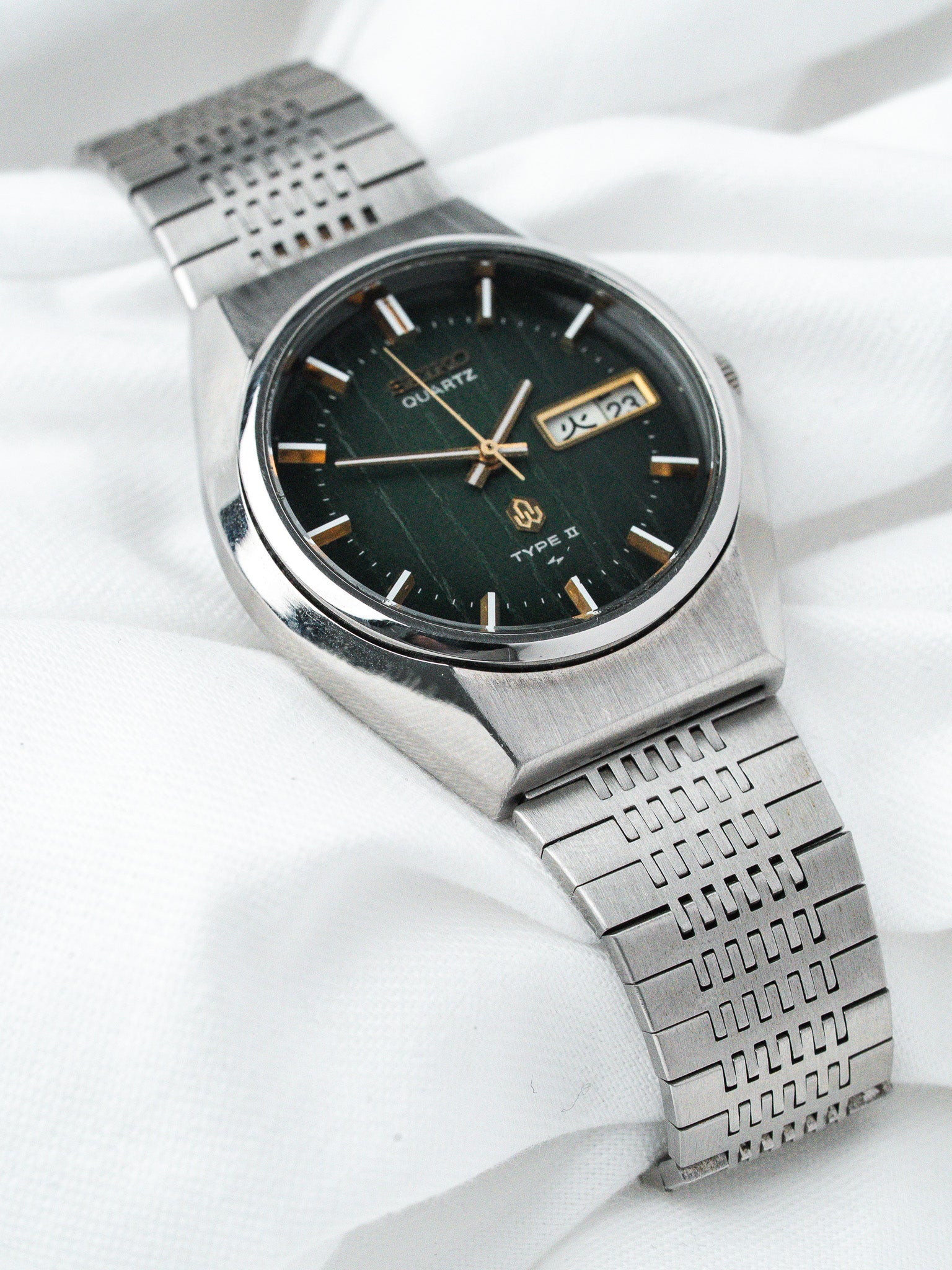Seiko Quartz Type II vintage watch with green dial, gold markers, steel bracelet on white fabric