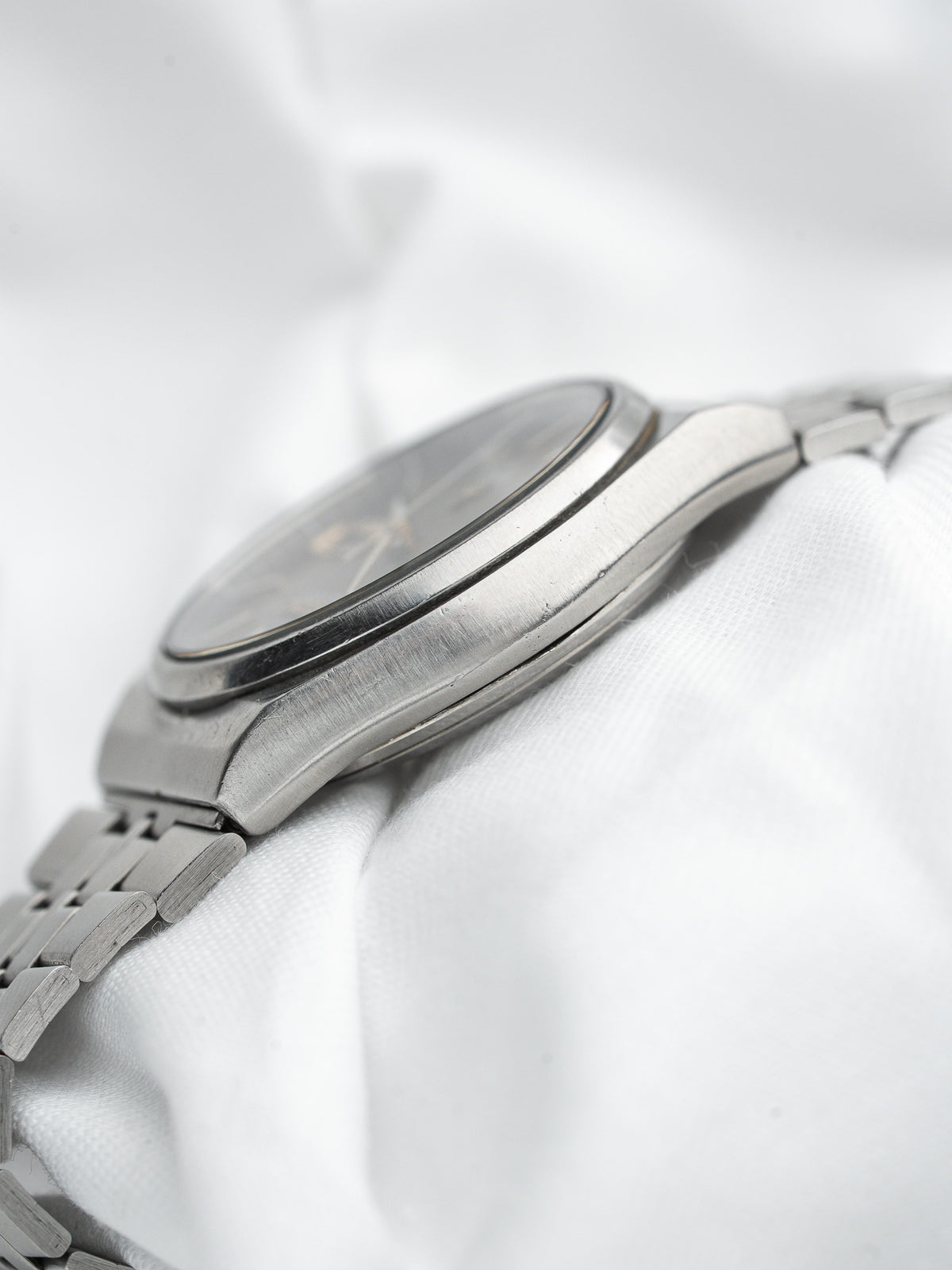 Vintage Omega watch with steel bracelet, dark dial, on white fabric