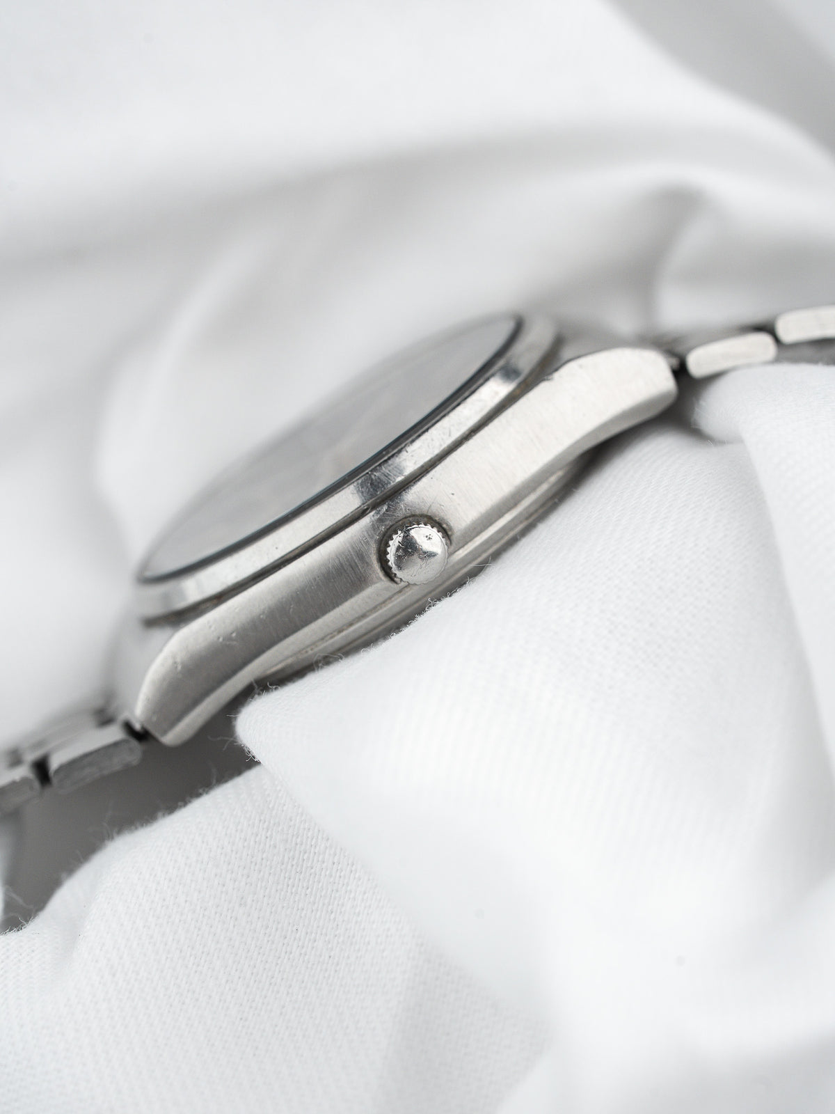 Vintage Omega watch side profile, stainless steel case, crown detail on white fabric