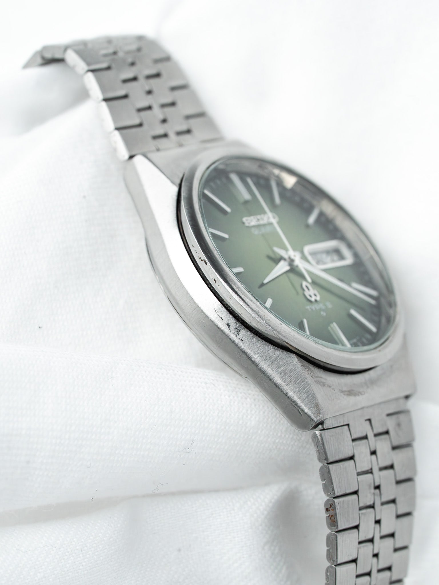 Seiko 5 vintage watch with green dial, steel bracelet, on white fabric background