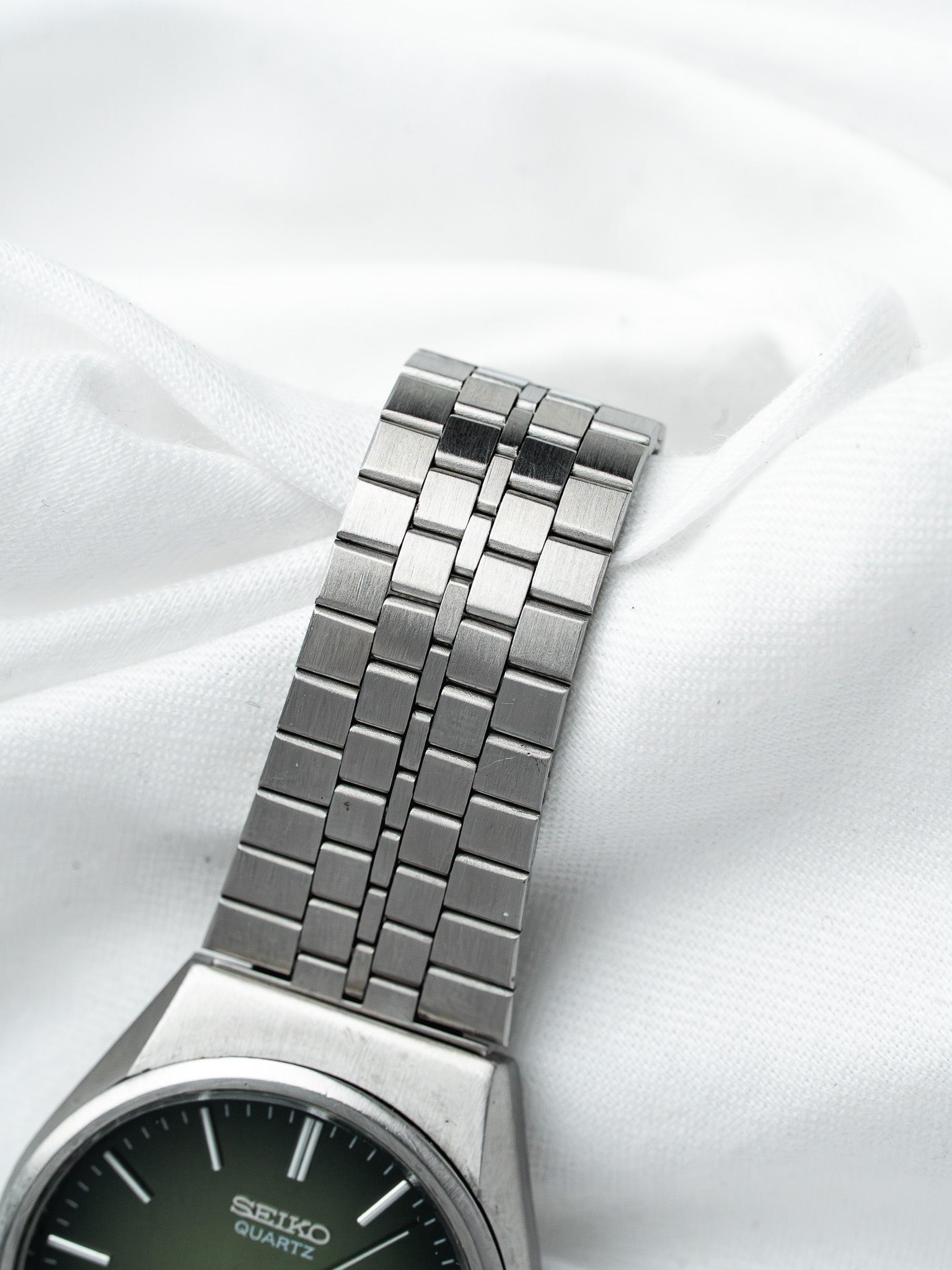 Seiko Quartz vintage watch with green dial and stainless steel bracelet on white fabric