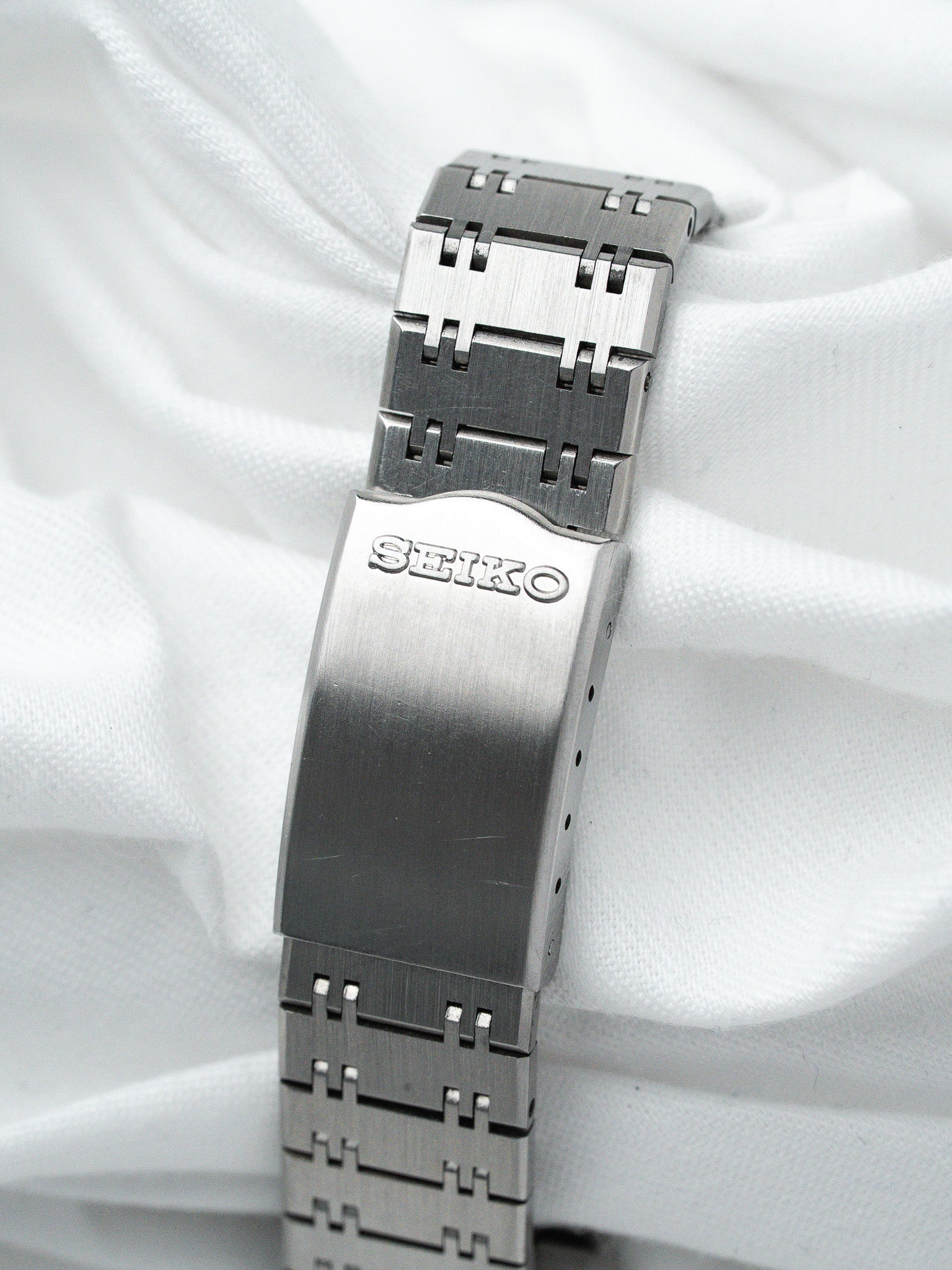 Seiko vintage watch bracelet in brushed stainless steel, clasp engraved SEIKO, on white fabric