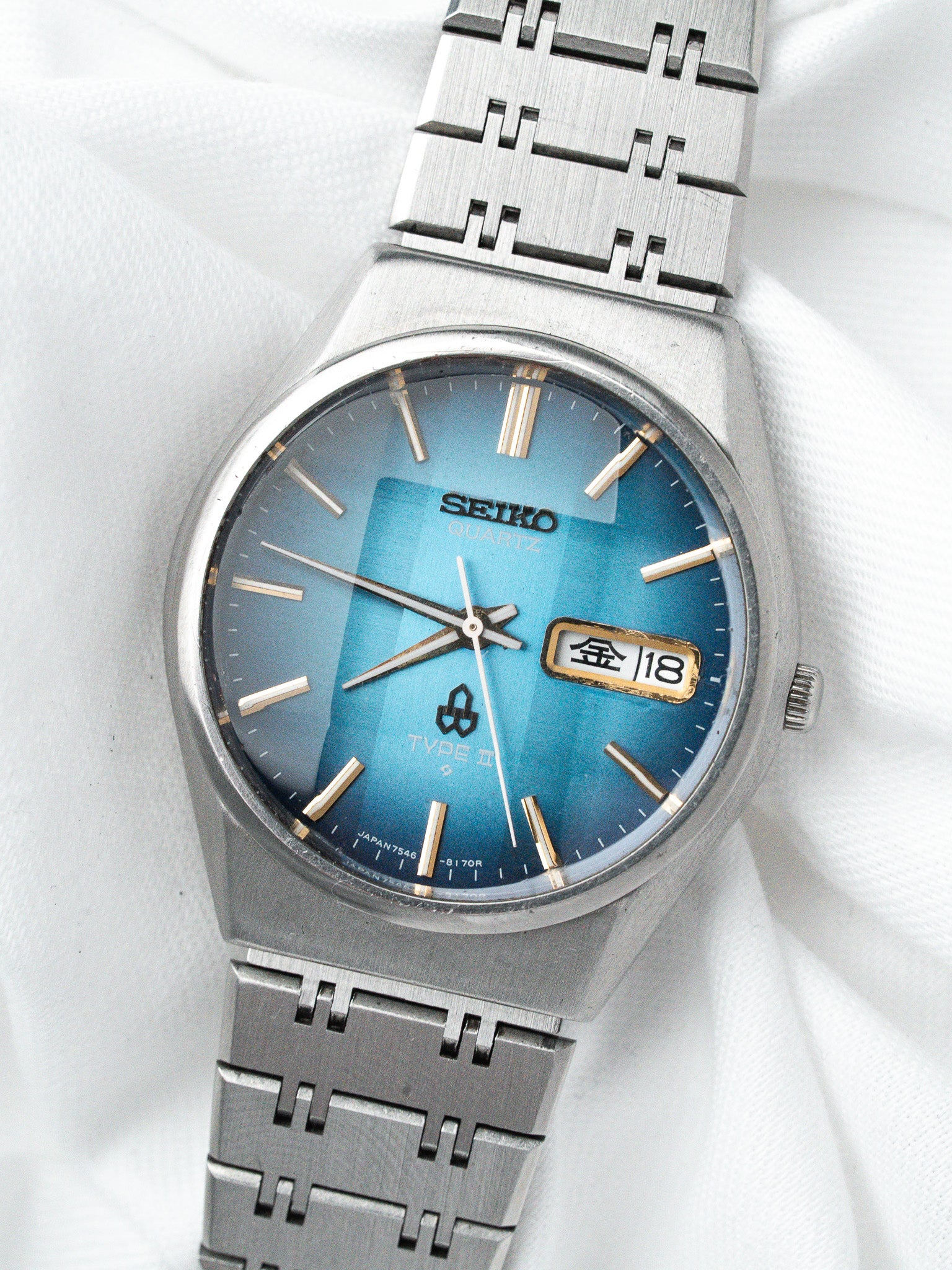 Seiko Quartz vintage watch with blue gradient dial, gold markers, and steel bracelet on white fabric