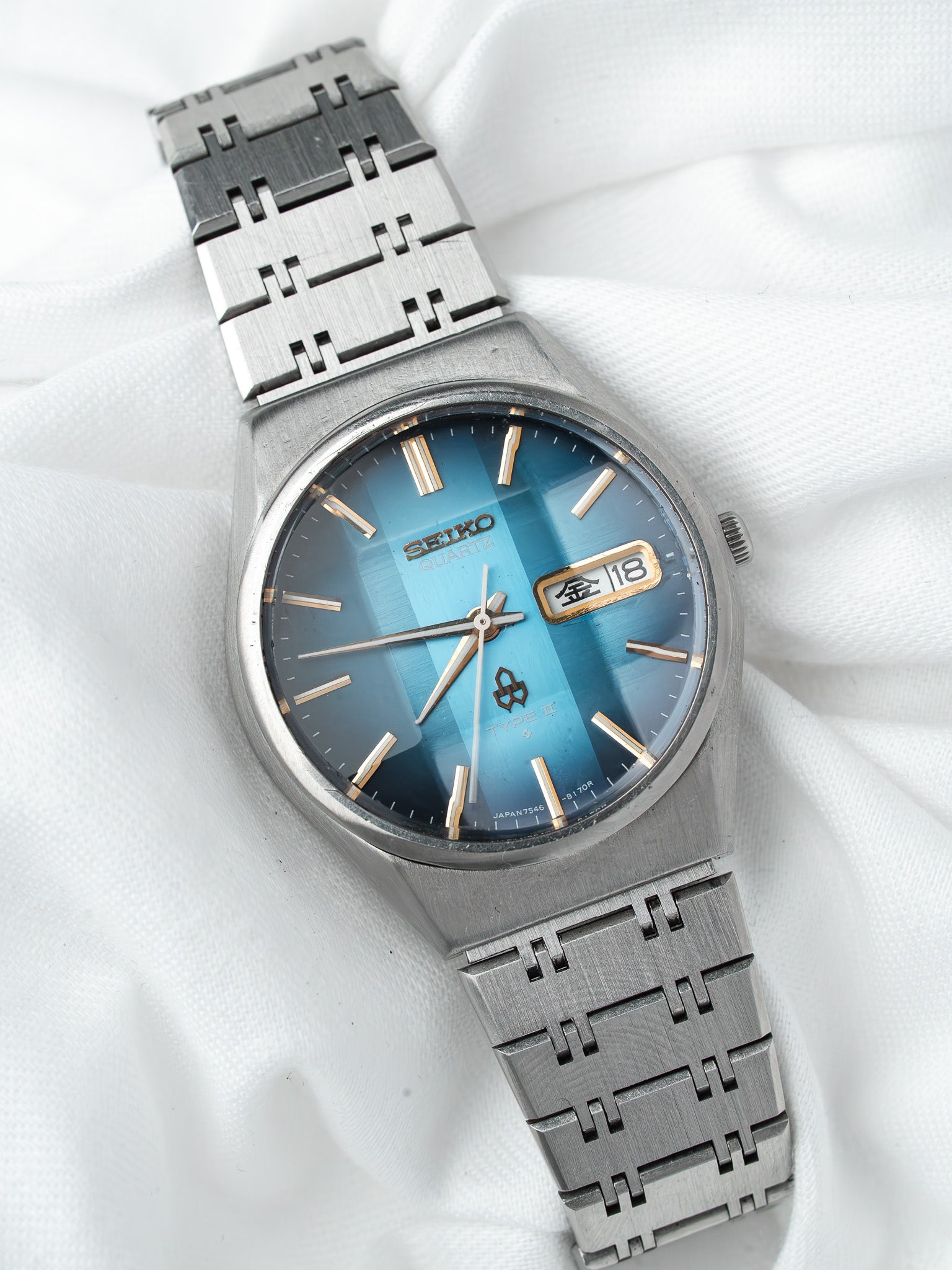 Seiko Quartz vintage watch with blue gradient dial, gold markers, and steel bracelet on white fabric