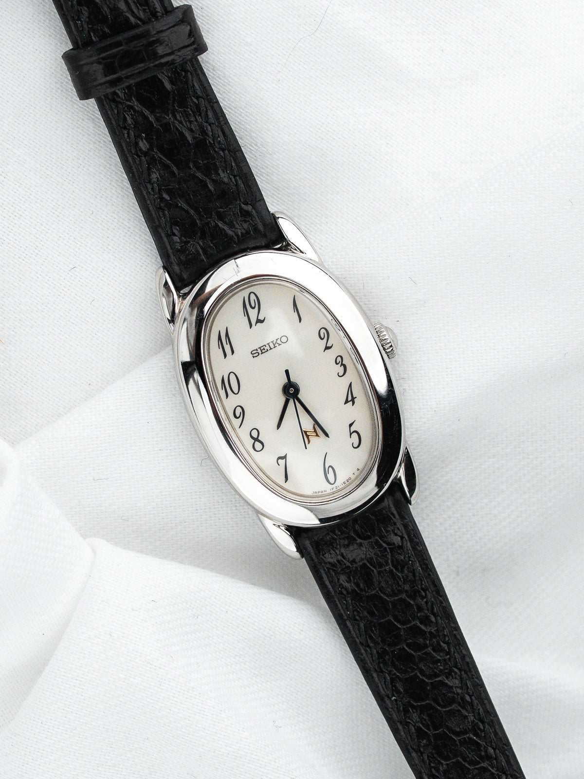 Montre Seiko vintage, boîtier ovale argenté, cadran blanc et bracelet en cuir noir