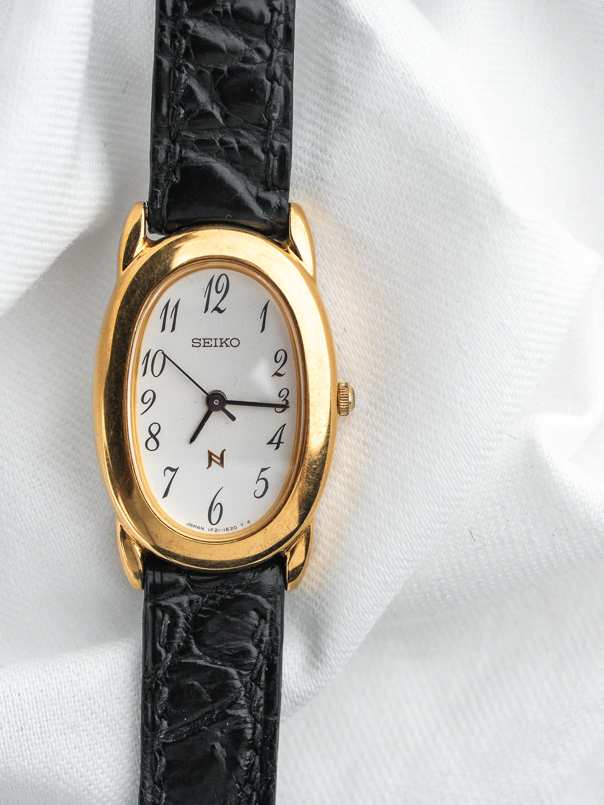 Montre Seiko vintage, boîtier ovale doré, cadran blanc et bracelet en cuir noir