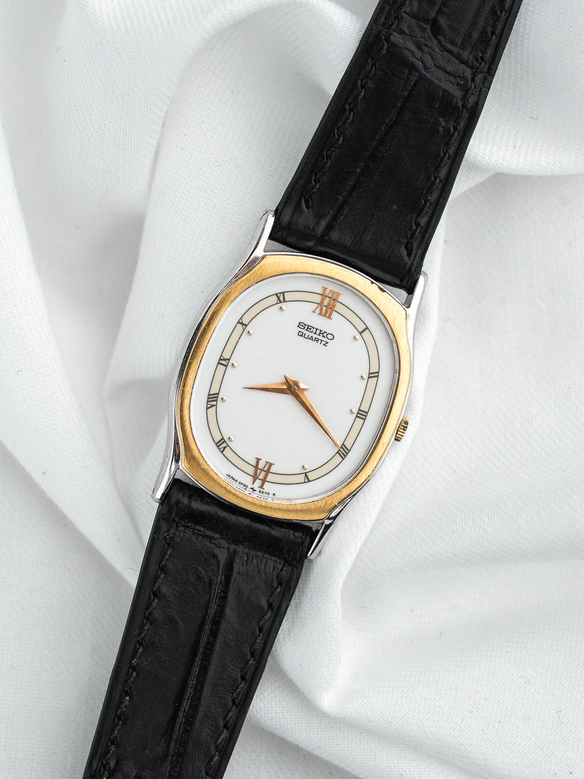 Montre Seiko Quartz vintage, boîtier ovale doré, cadran blanc et bracelet cuir noir