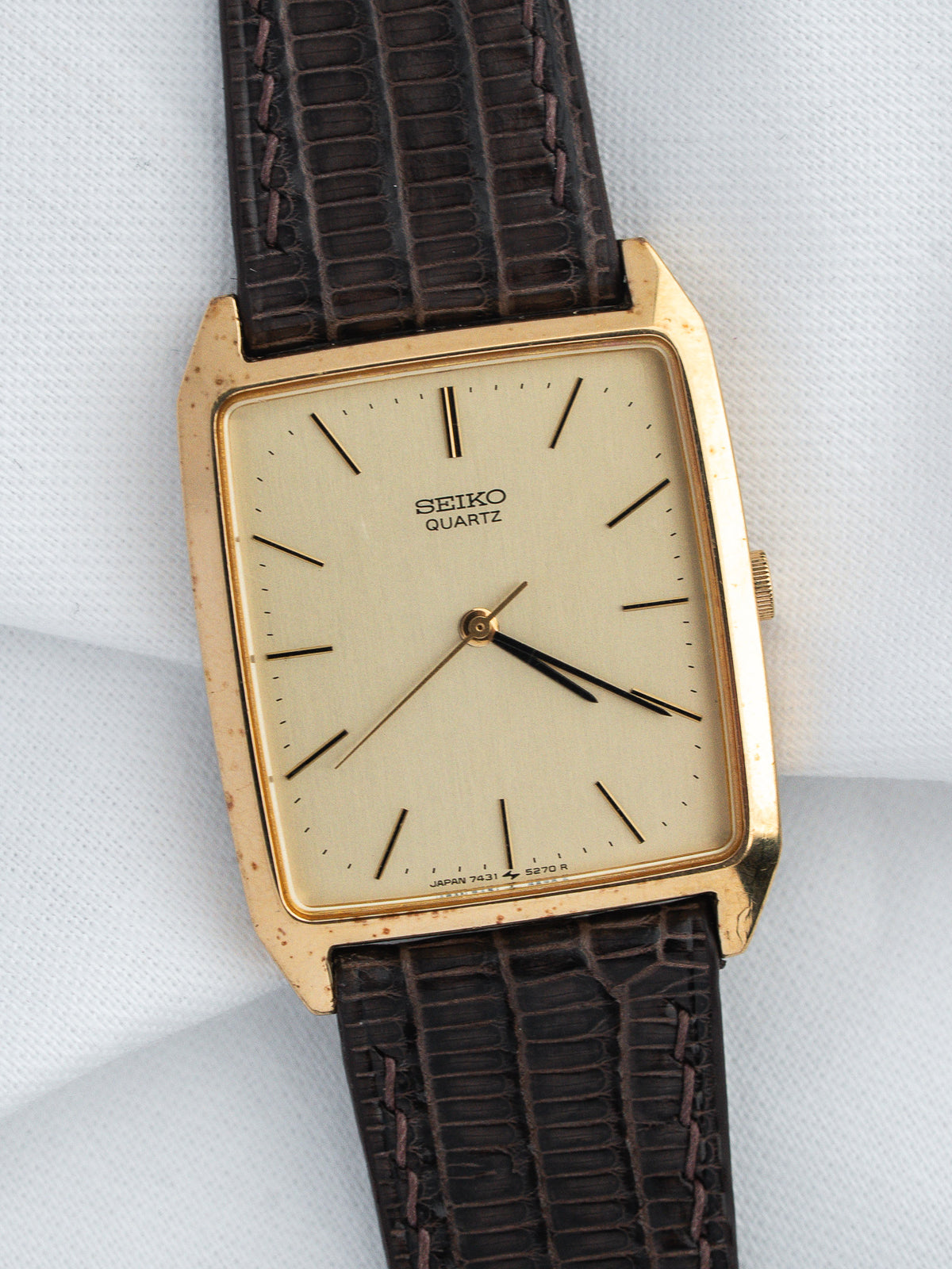 Vintage Seiko Quartz watch with gold case, cream dial, and brown textured strap on white background