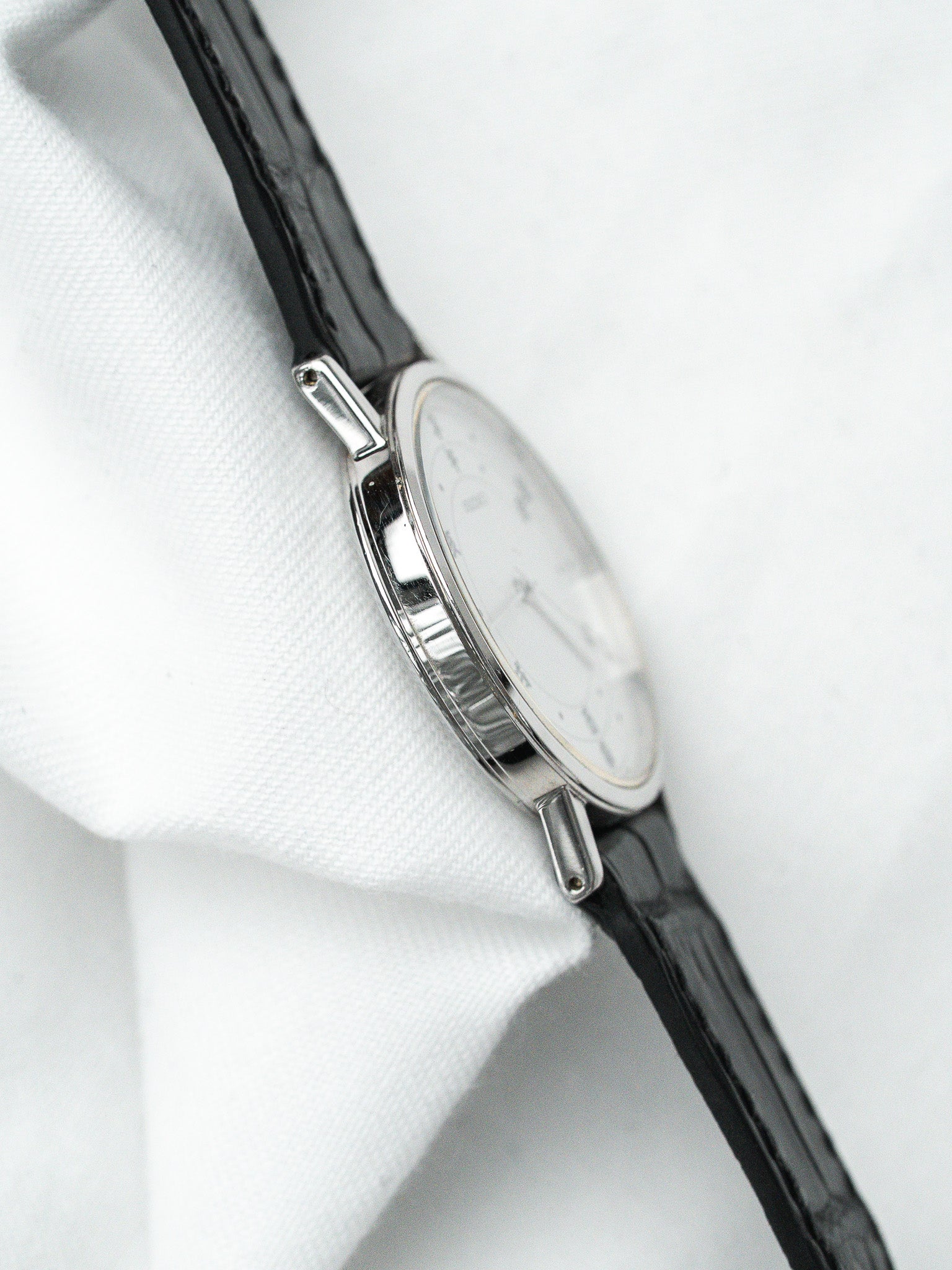 Vintage Universal Genève watch with silver case, white dial, black leather strap on white fabric