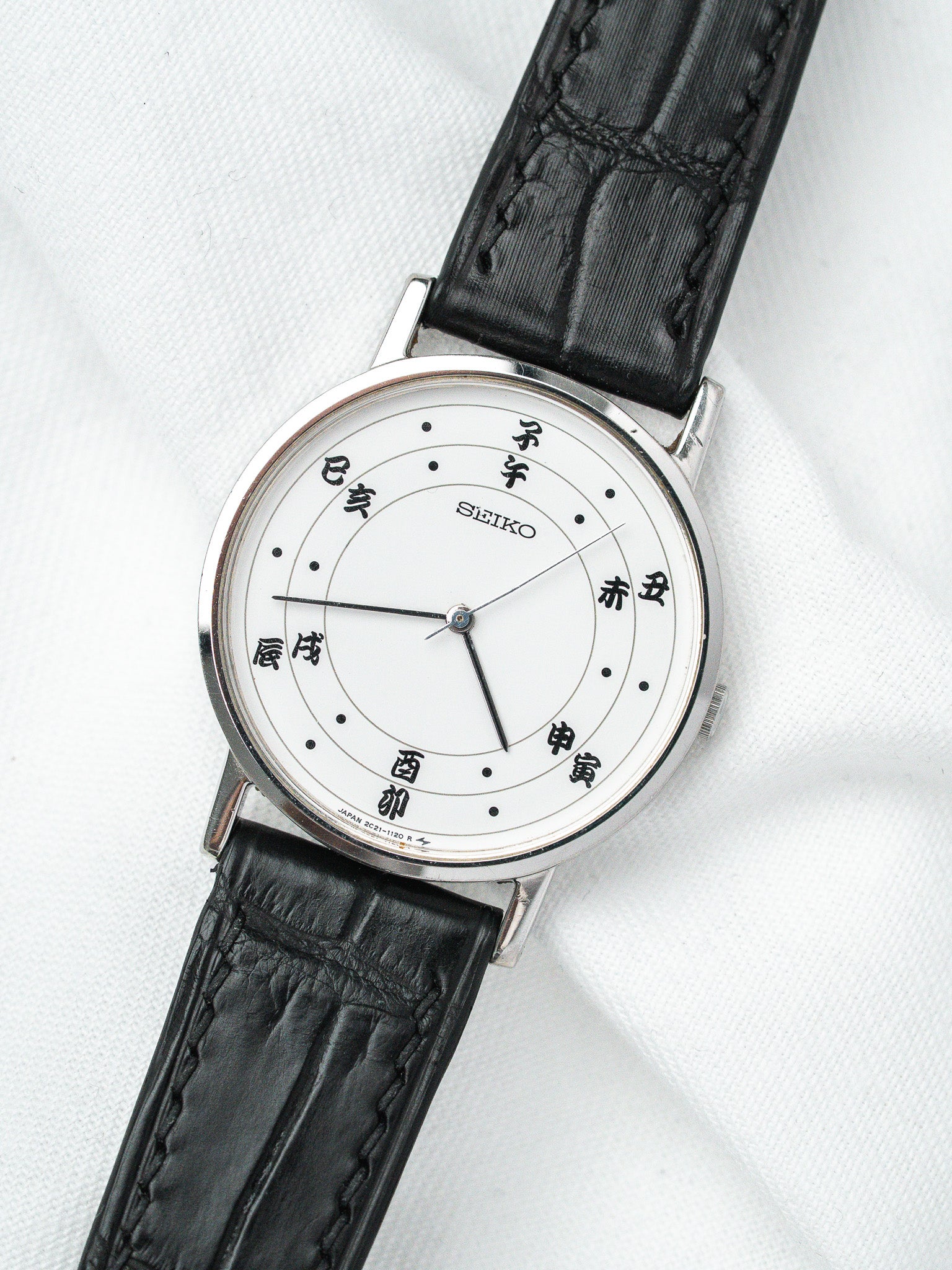 Seiko vintage watch with white dial, Japanese characters, black leather strap on white fabric