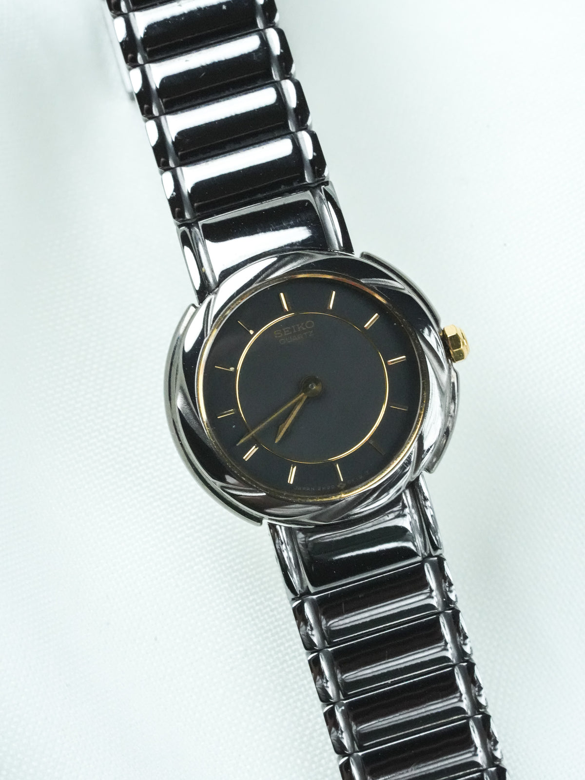 Seiko vintage quartz watch with black dial, gold accents, and metallic bracelet on white background