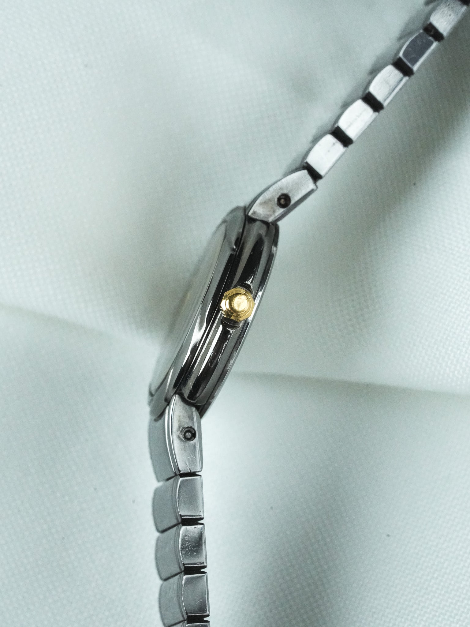 Vintage Omega watch with steel bracelet and gold crown, side view on white