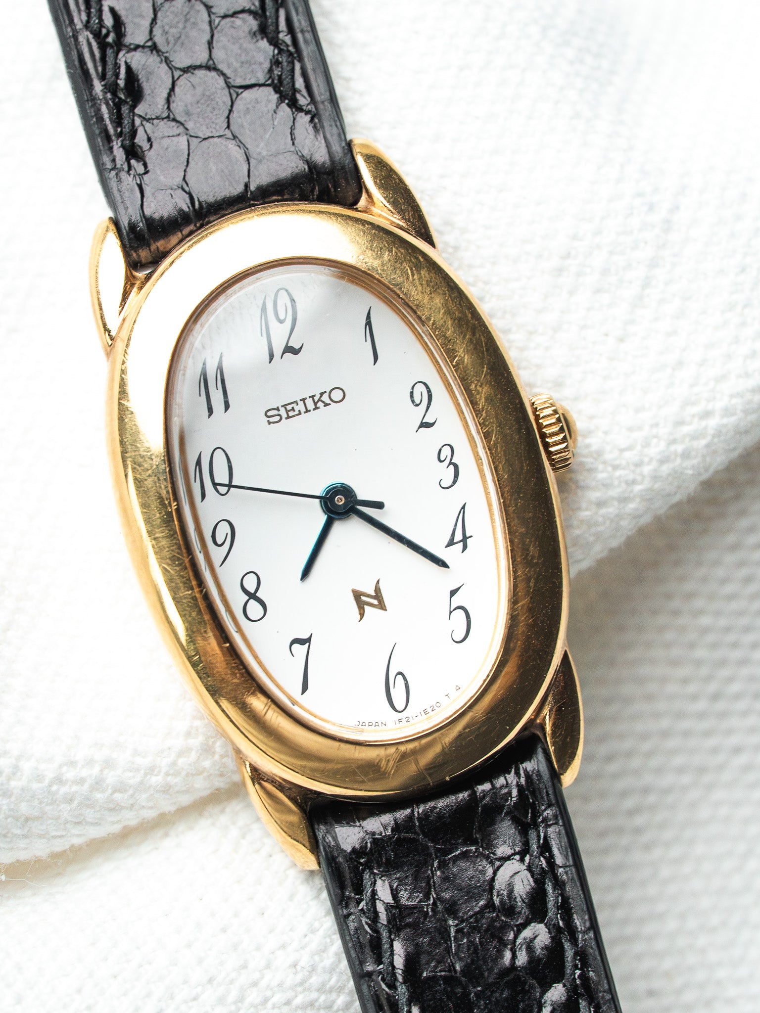 Seiko vintage watch with gold case, white dial, black alligator strap on white fabric