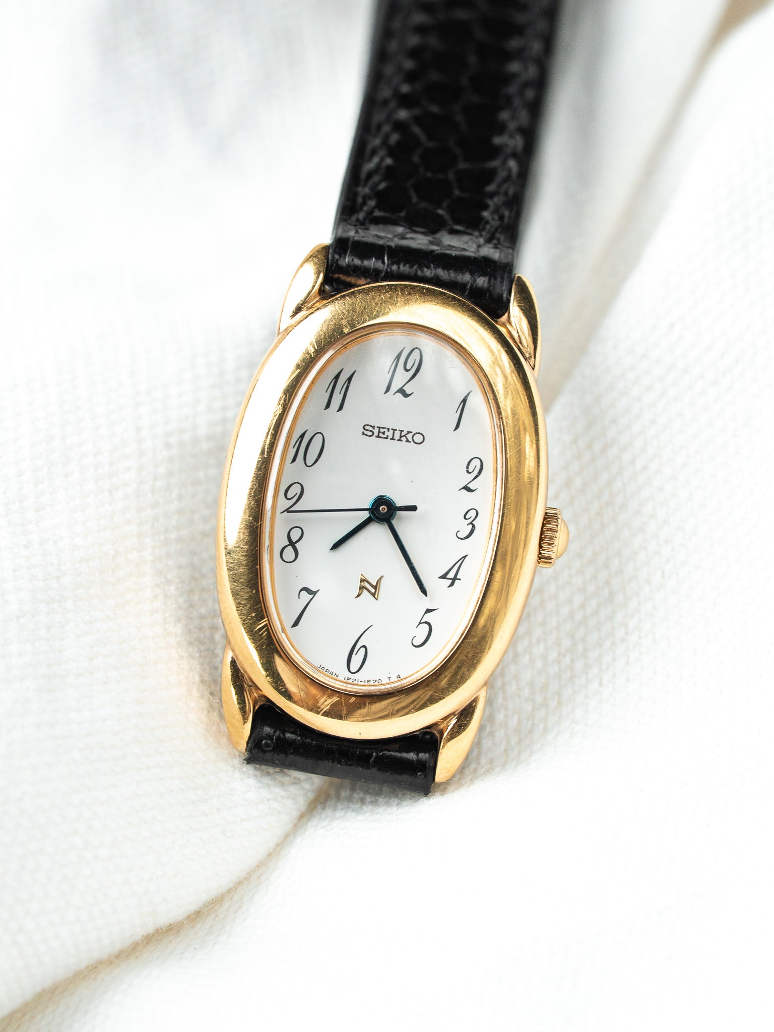 Seiko vintage watch with gold case, white dial, black leather strap on white fabric