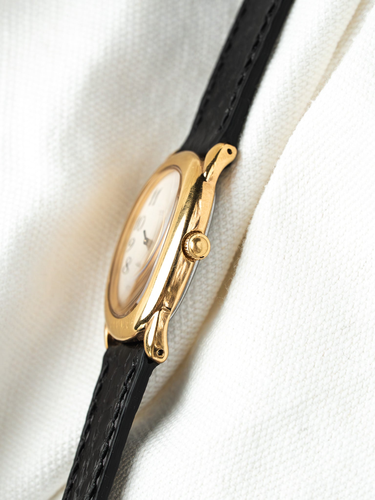 Cartier vintage watch with gold case, white dial, black leather strap on fabric