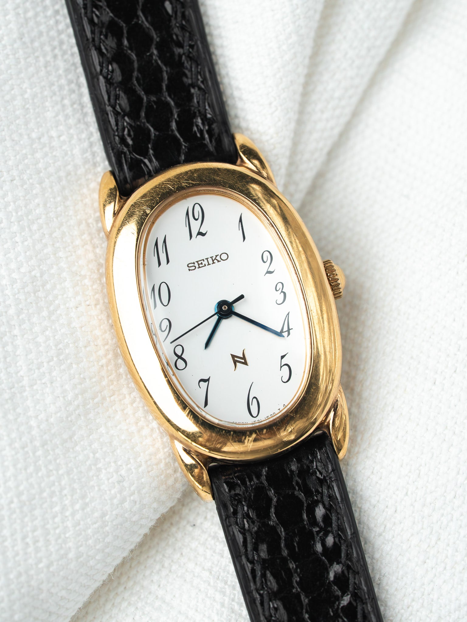 Seiko vintage watch with gold case, white dial, black alligator strap on white fabric