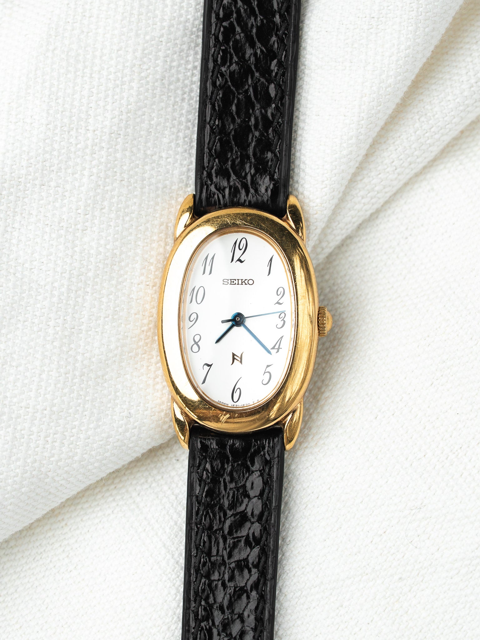 Seiko vintage watch with gold case, white dial, black leather strap on white fabric