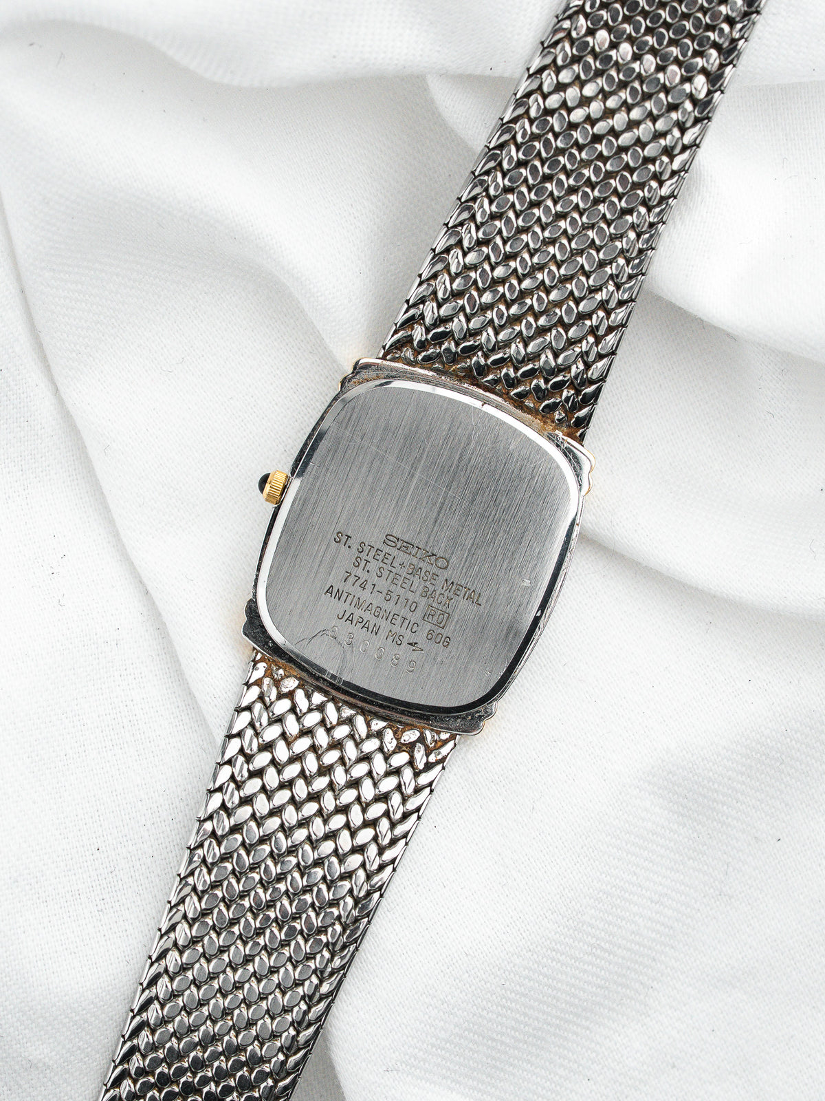 Dos d'une montre Seiko vintage en acier avec bracelet maille milanaise sur fond blanc
