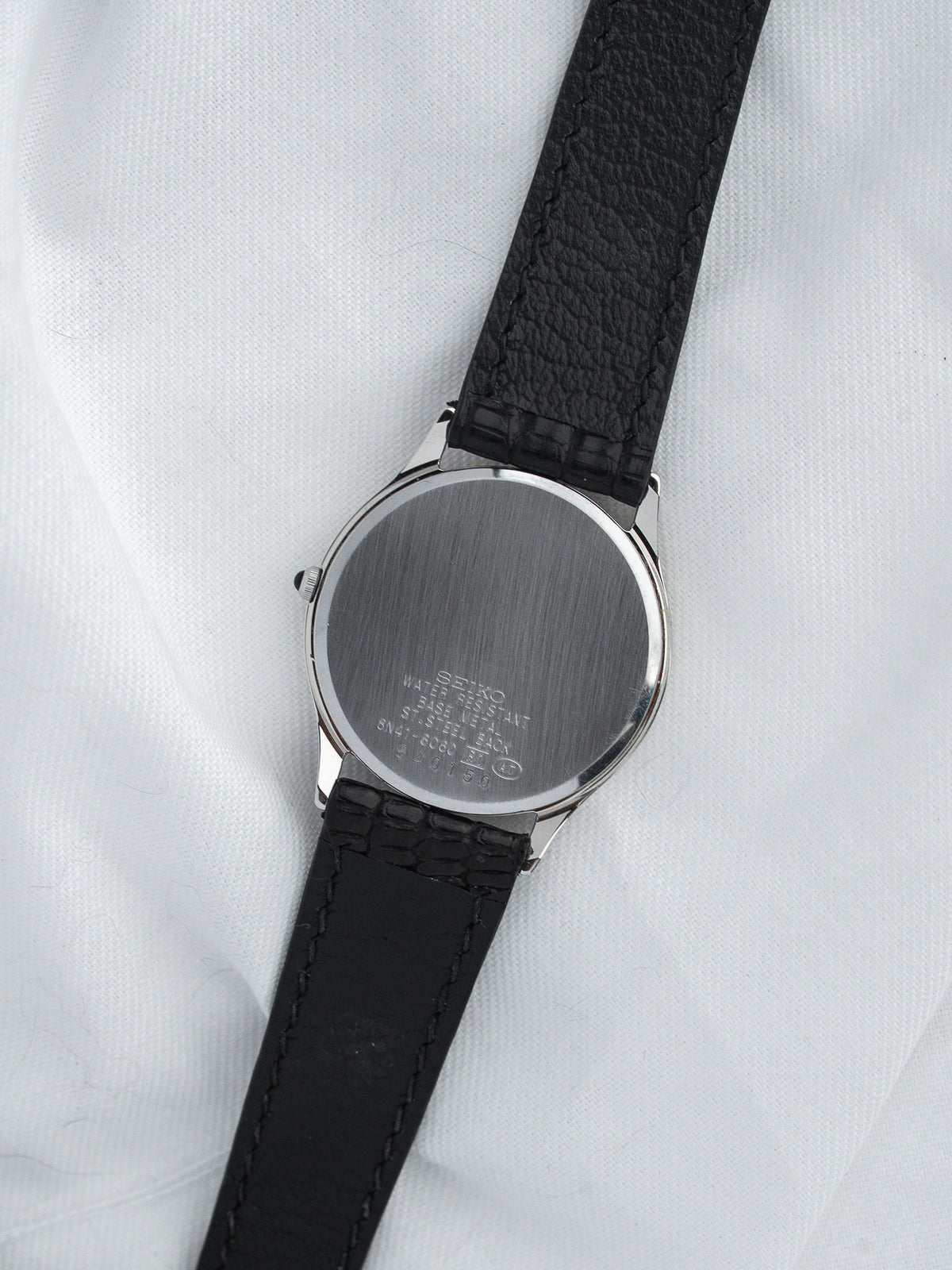 Seiko vintage watch with stainless steel case and black leather strap, back view on white fabric