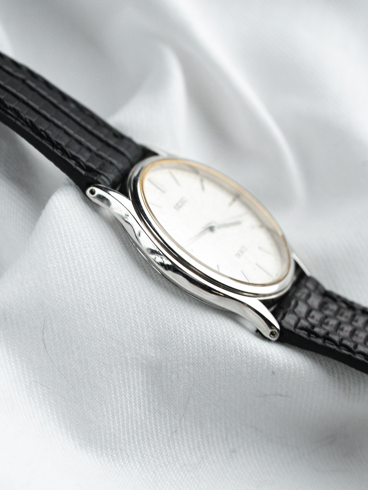 Vintage Omega watch with white dial, black leather strap, and silver case