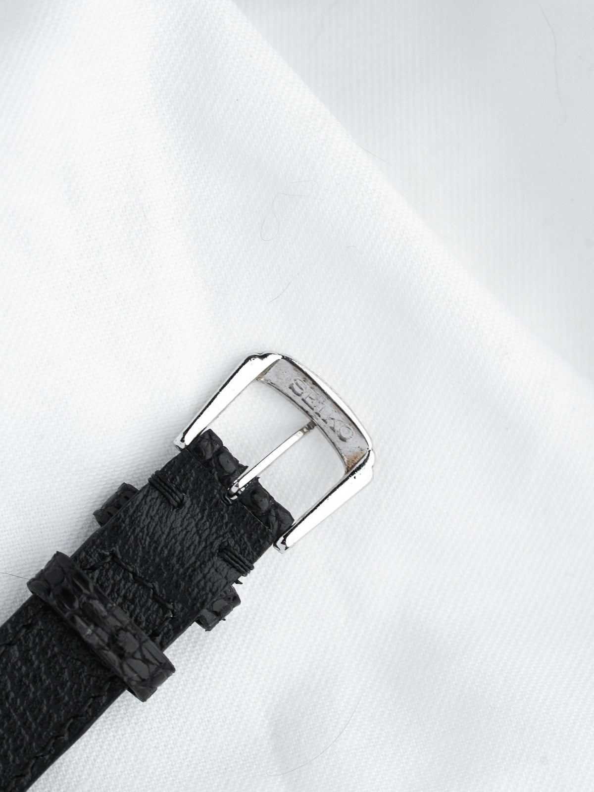 Seiko watch strap with black textured leather and silver buckle on white fabric