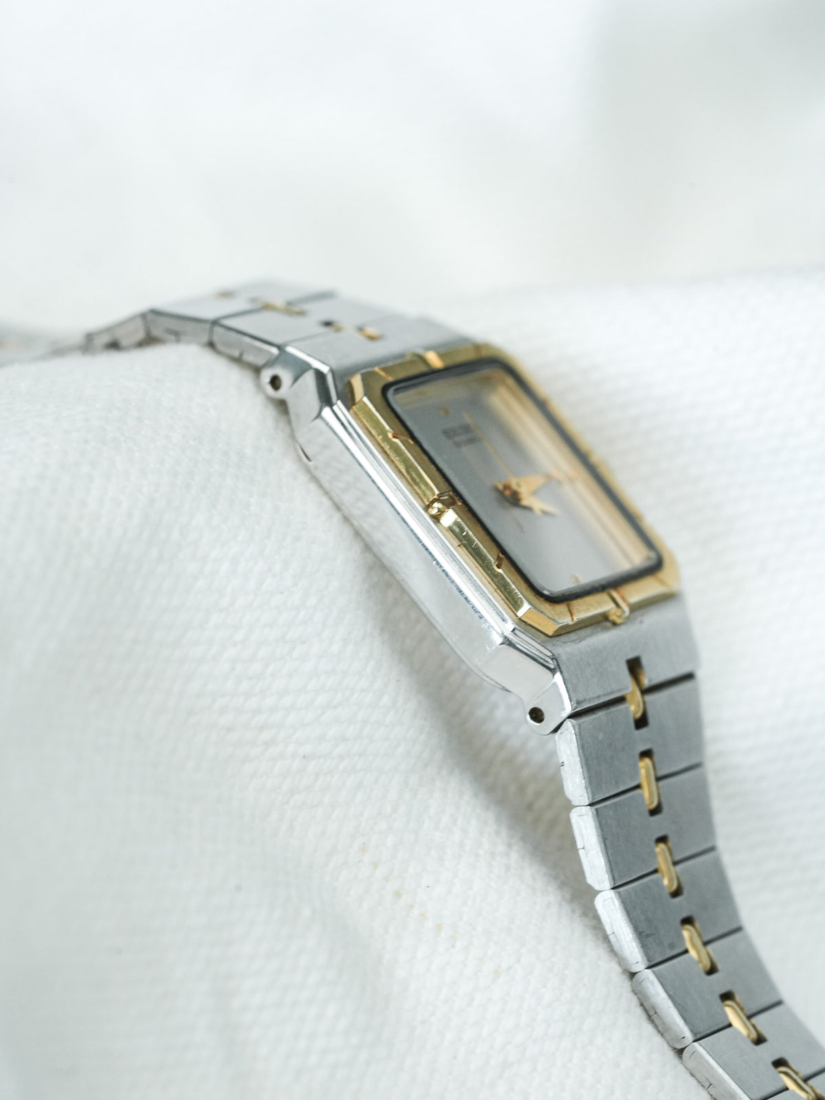 Vintage Seiko rectangular watch with gold accents and silver bracelet on white fabric