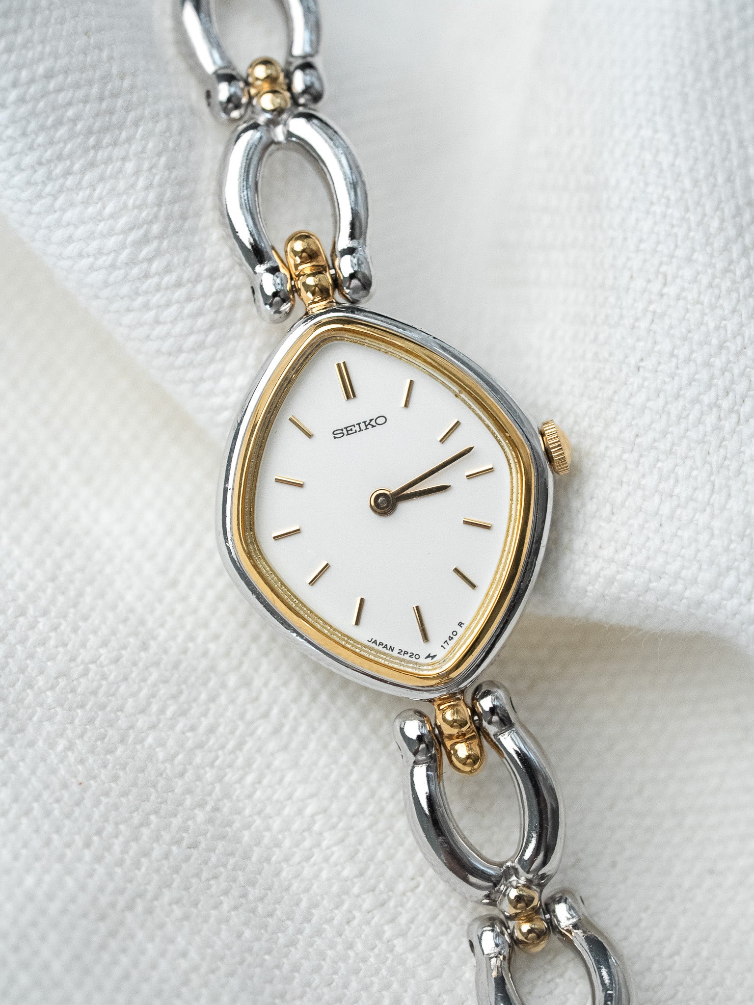 Seiko vintage watch with white dial, gold accents, and two-tone bracelet on textured white background