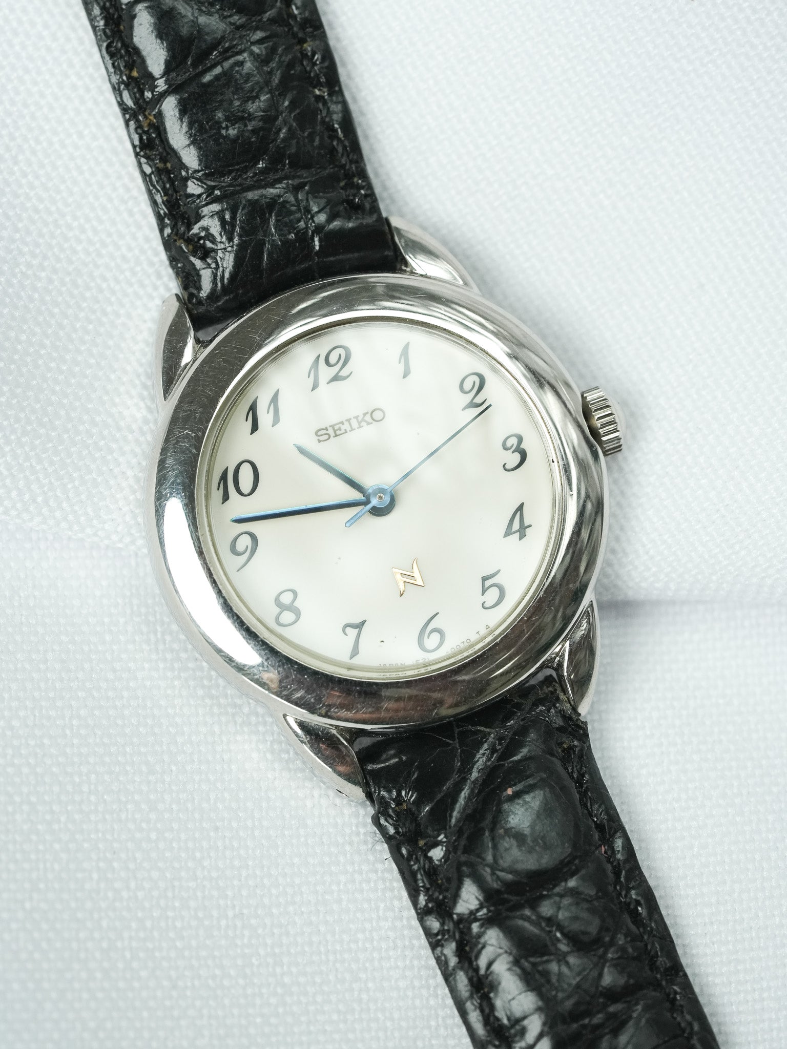 Vintage Seiko wristwatch with white dial, black alligator strap, and silver case on white background