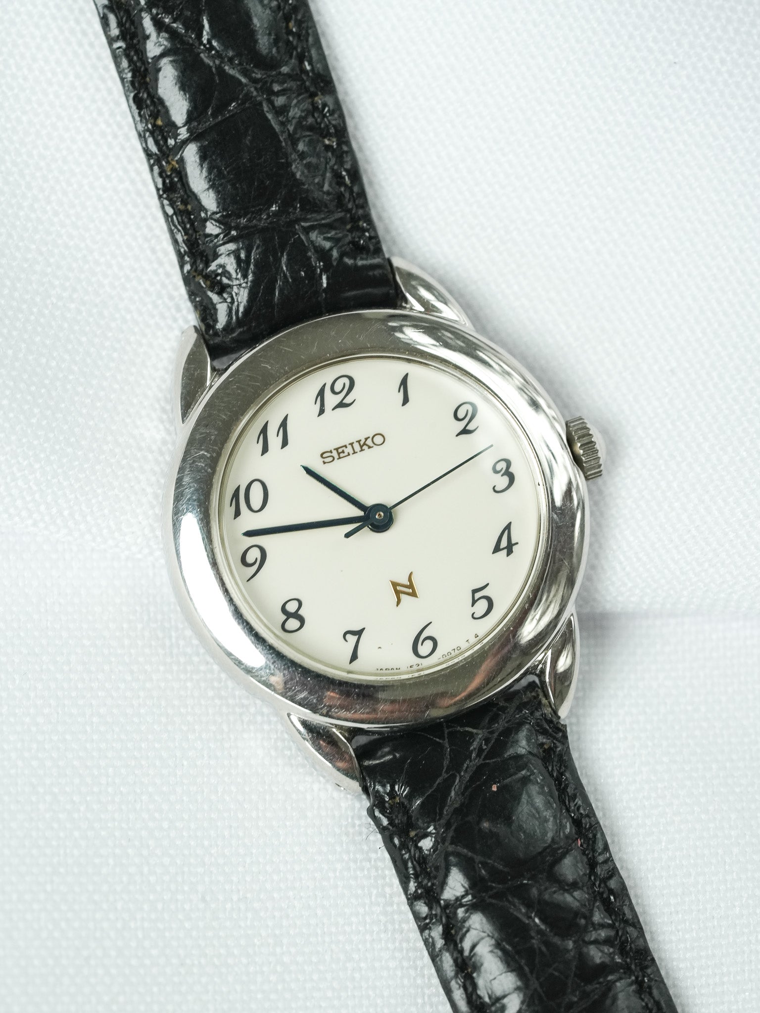 Seiko vintage watch with white dial, black leather strap, and silver case on white background