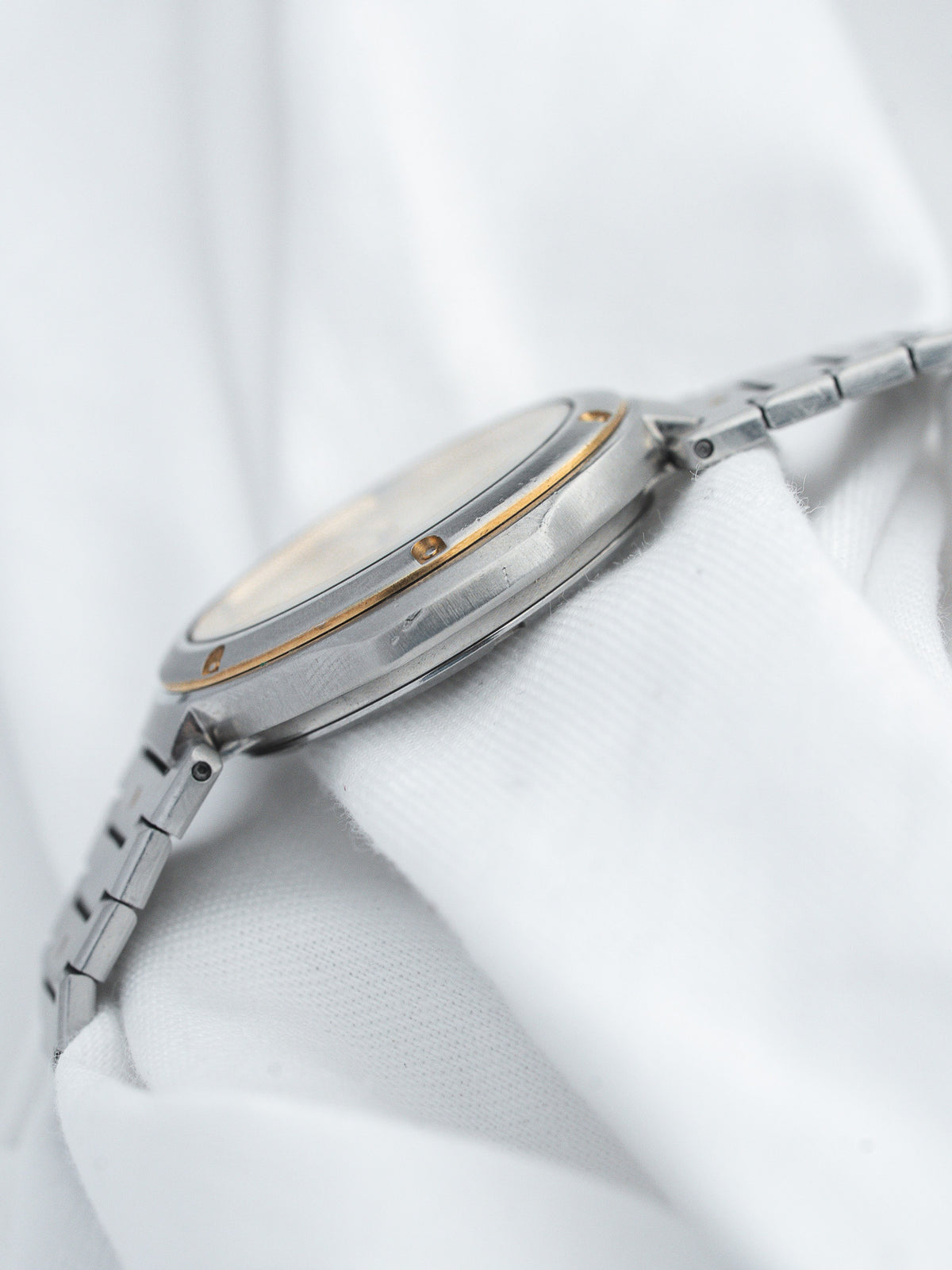 Vintage Omega watch with steel case, gold accents, and metal bracelet on white fabric