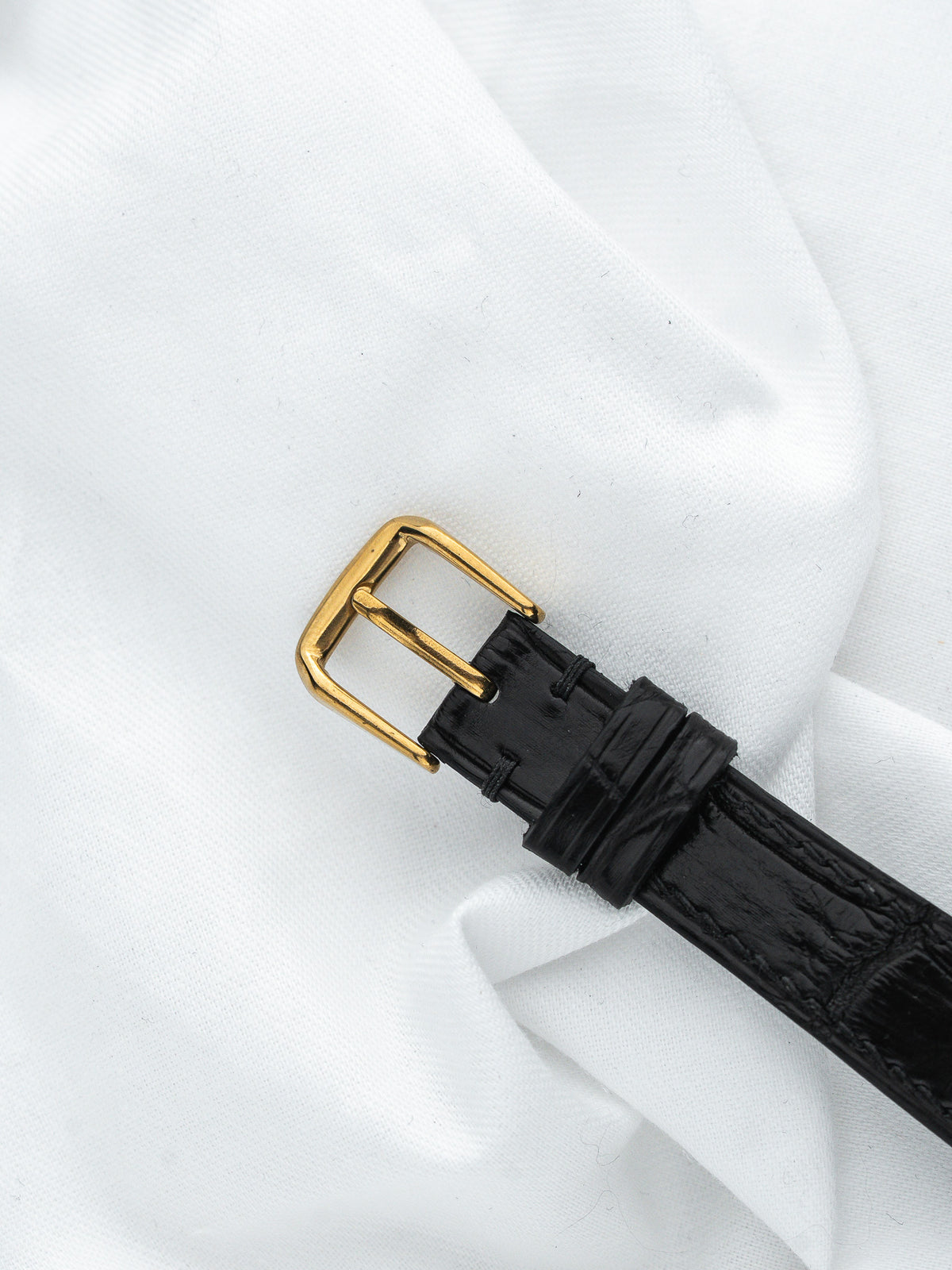 Boucle de montre dorée sur un bracelet en cuir noir sur fond blanc
