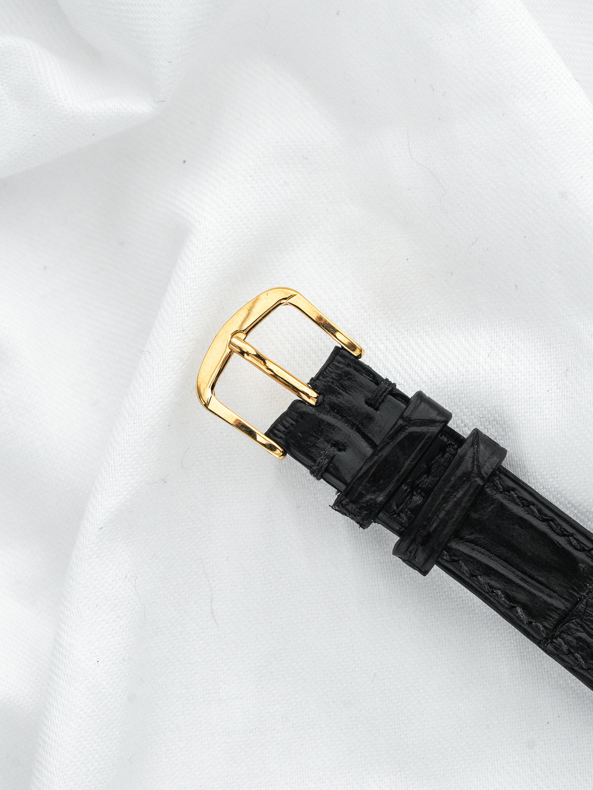 Boucle de montre vintage en or avec bracelet en cuir noir sur fond blanc