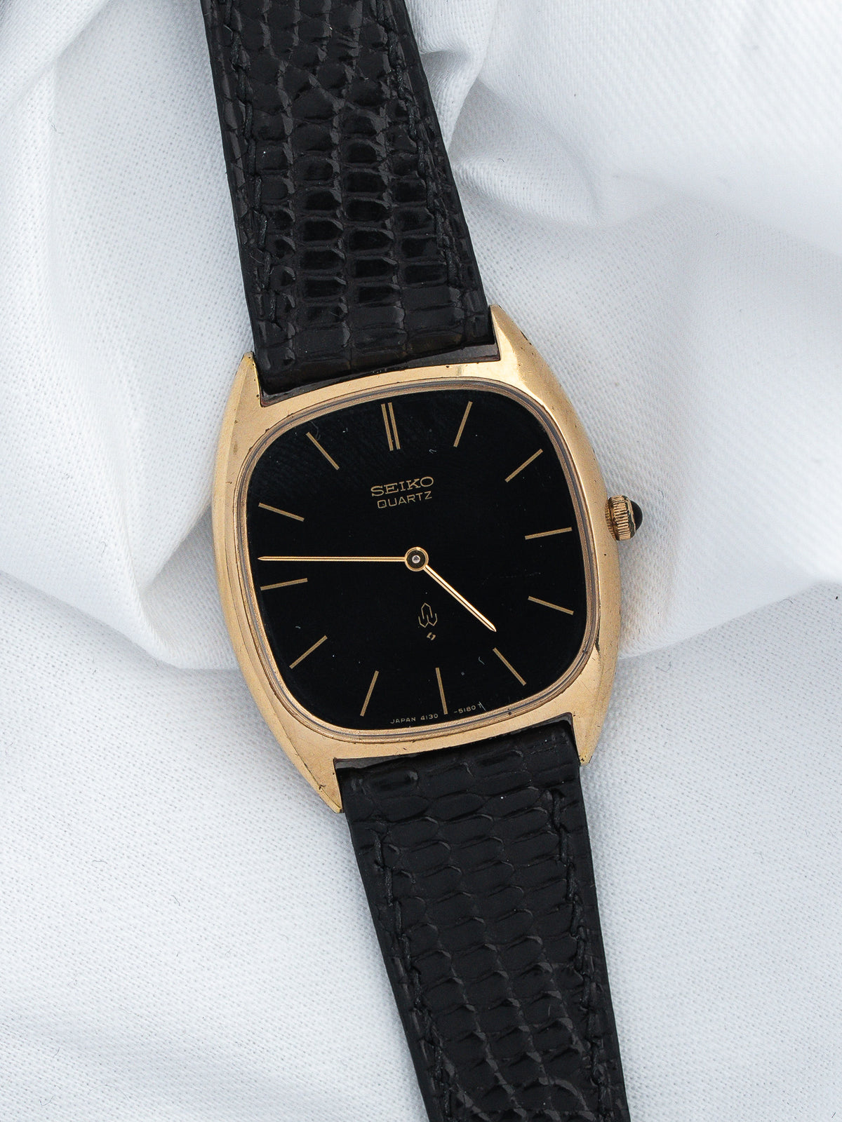Seiko Quartz vintage watch with gold case, black dial, and textured black strap on white fabric
