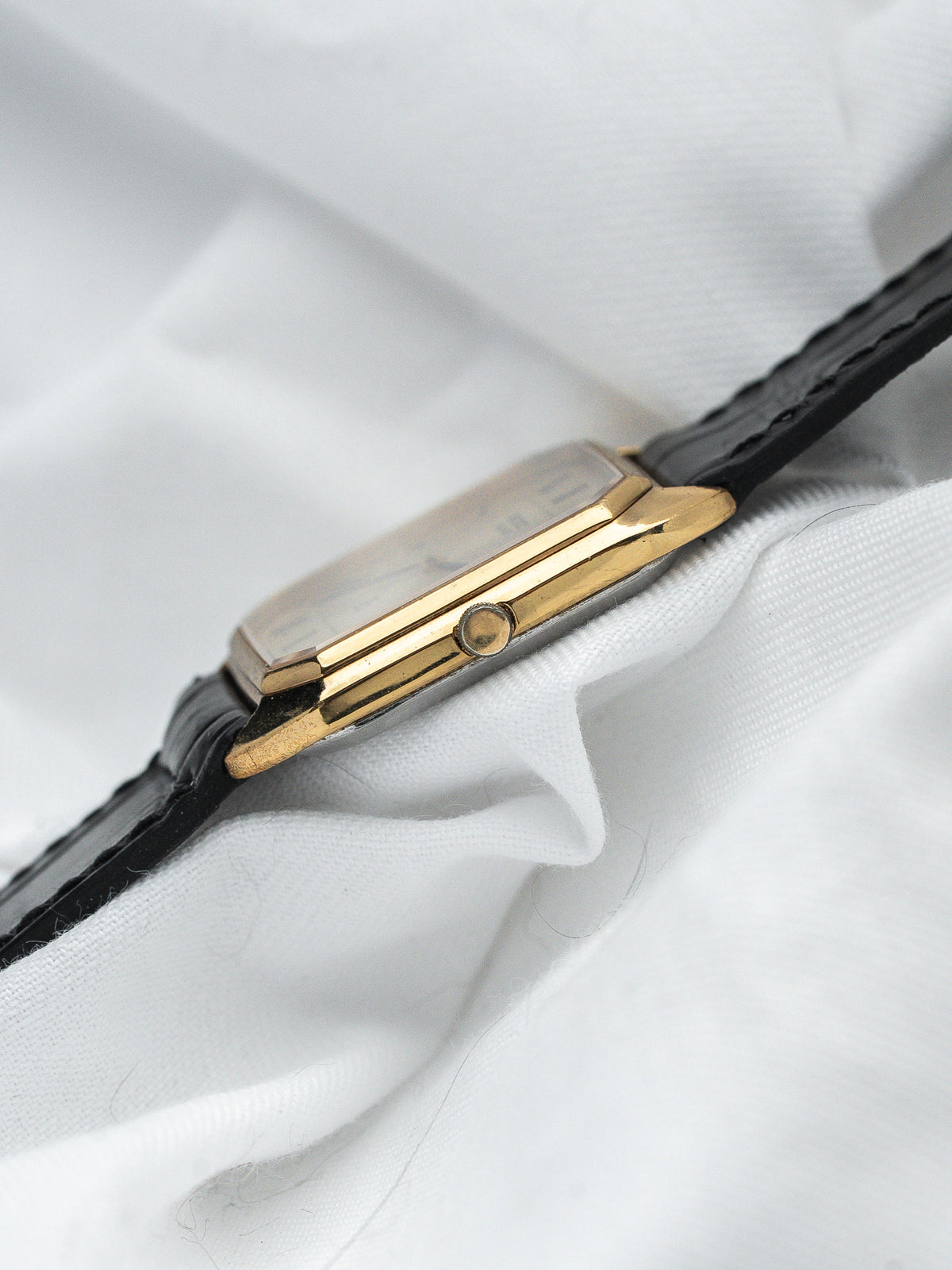 Vintage Cartier watch with gold case and black leather strap on white fabric