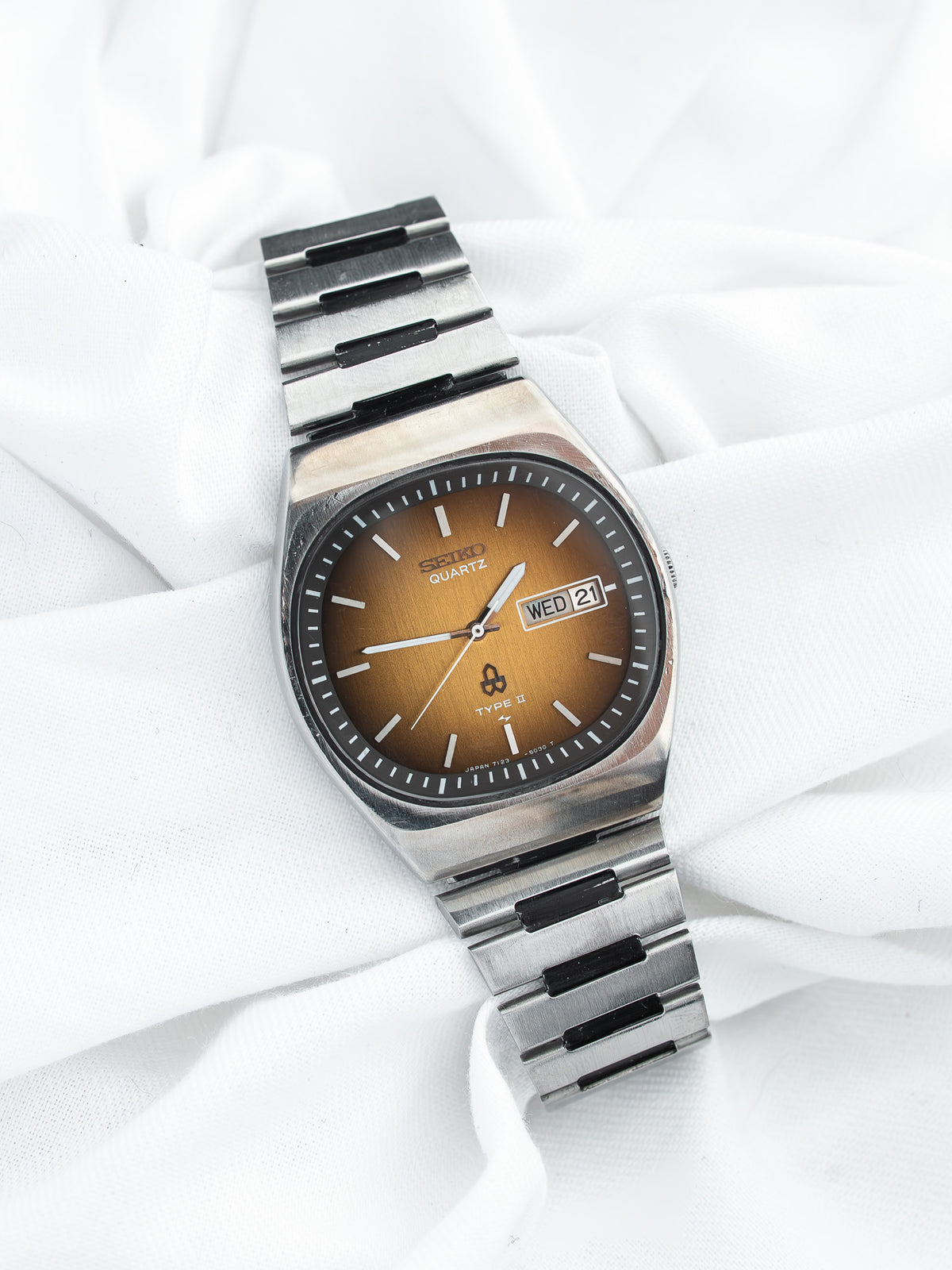 Montre Seiko Quartz vintage en acier, cadran marron et bracelet métallique sur tissu blanc