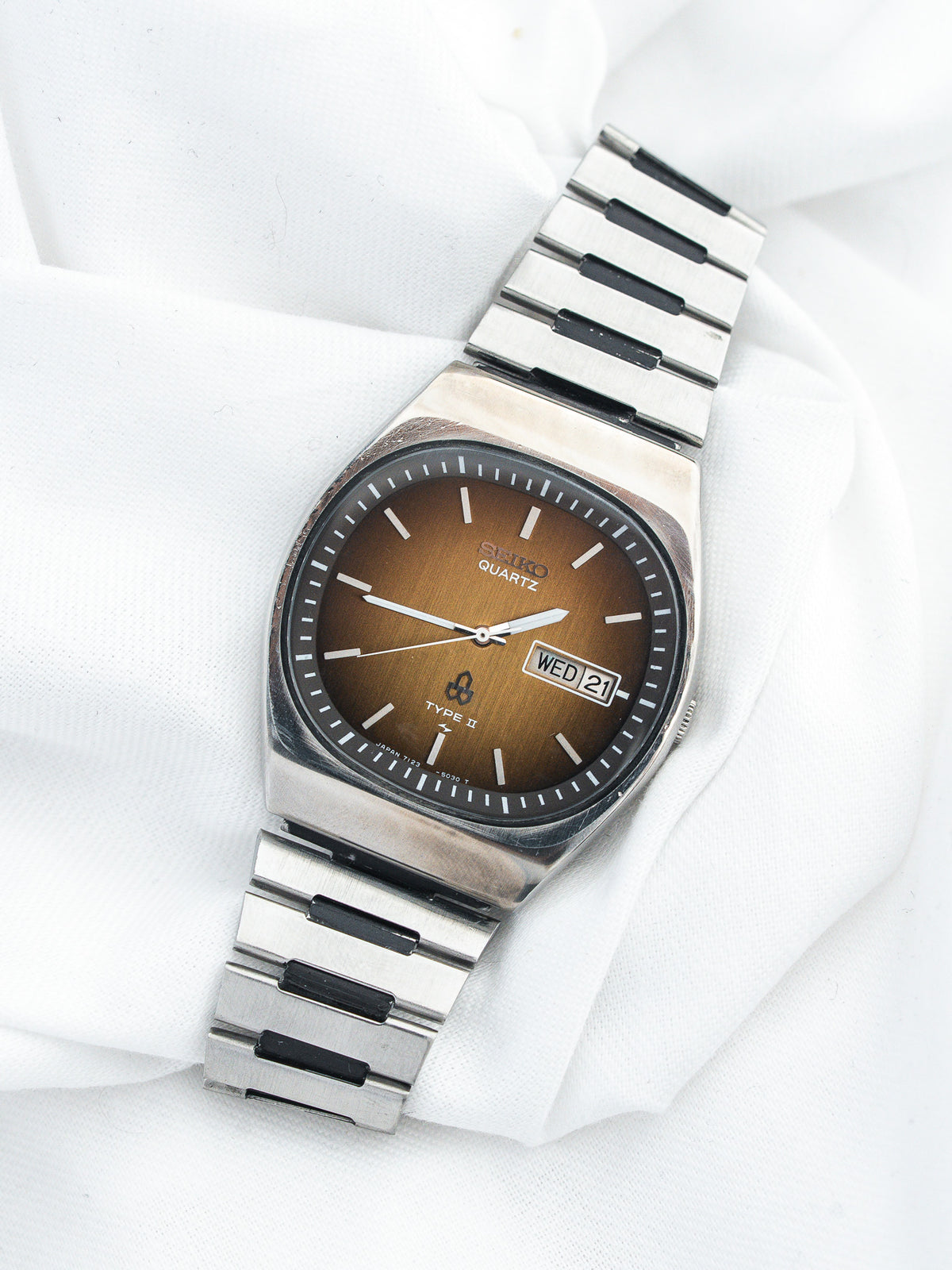 Montre Seiko Quartz vintage en acier, cadran marron et bracelet métallique, fond blanc