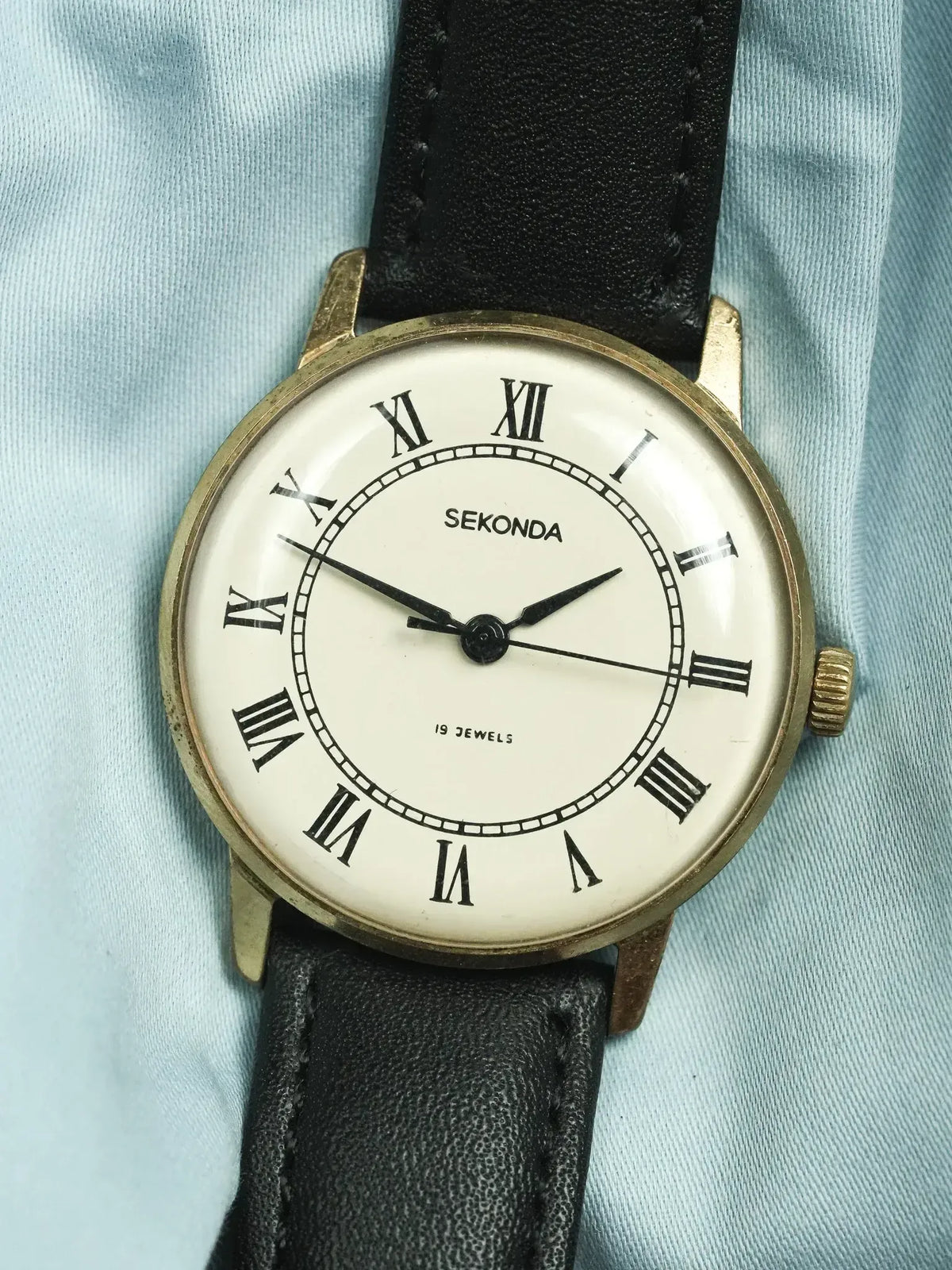 Vintage Sekonda watch with gold case, white dial, Roman numerals, black leather strap