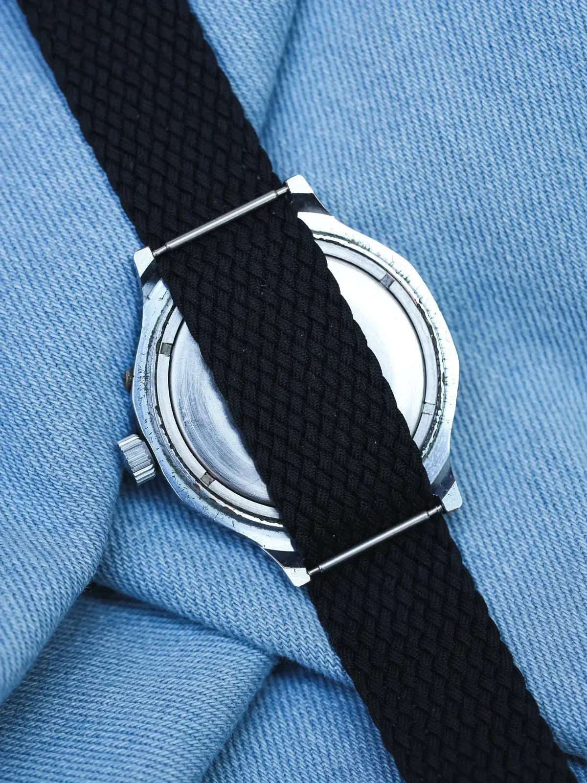 Vintage watch with black fabric strap and silver case on blue fabric