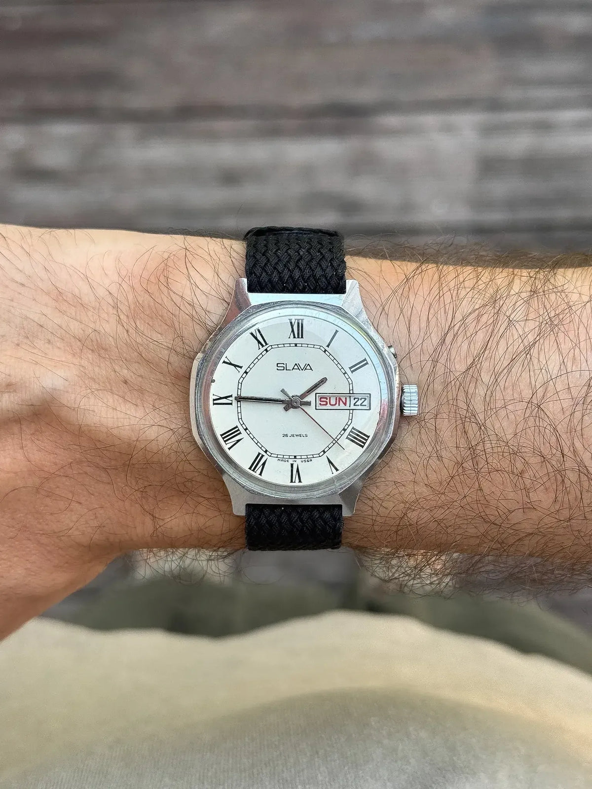 Slava vintage watch with white dial, Roman numerals, black fabric strap worn on wrist