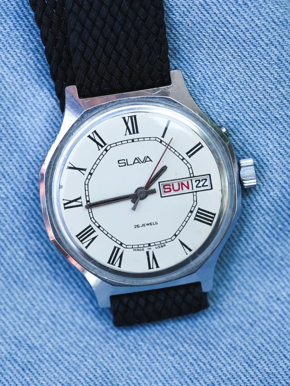 Slava vintage watch with white dial, Roman numerals, black braided strap on denim
